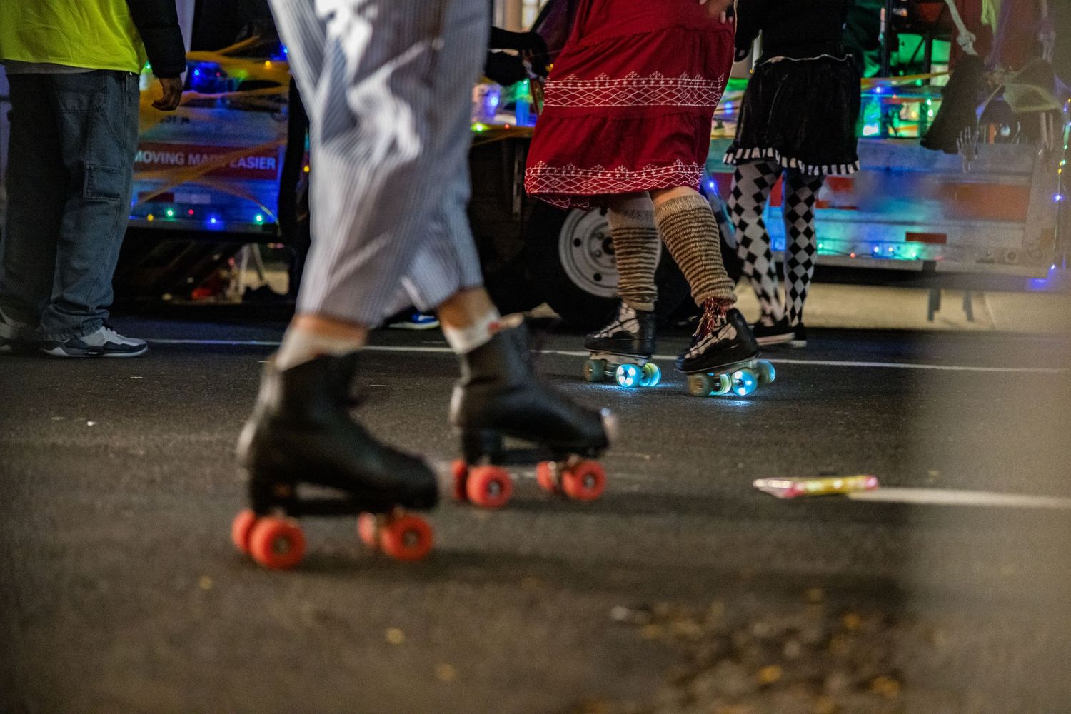 Roller skaters wearing colorful outfits skating on street during nighttime event.