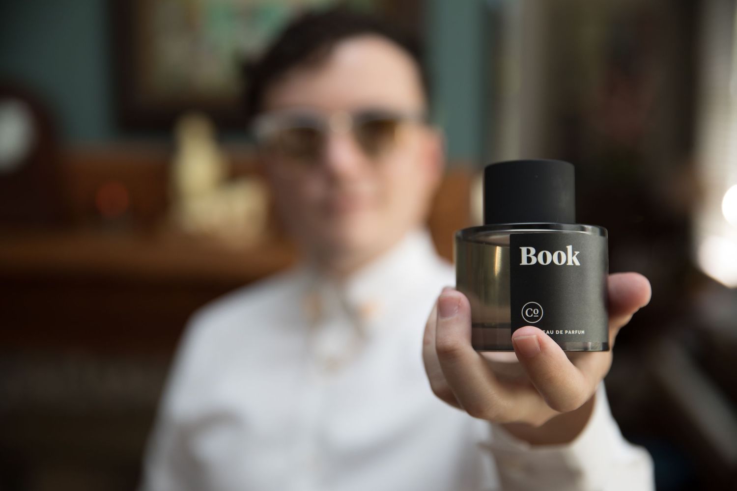Person holds a bottle of Book perfume in focus against a blurred indoor background.