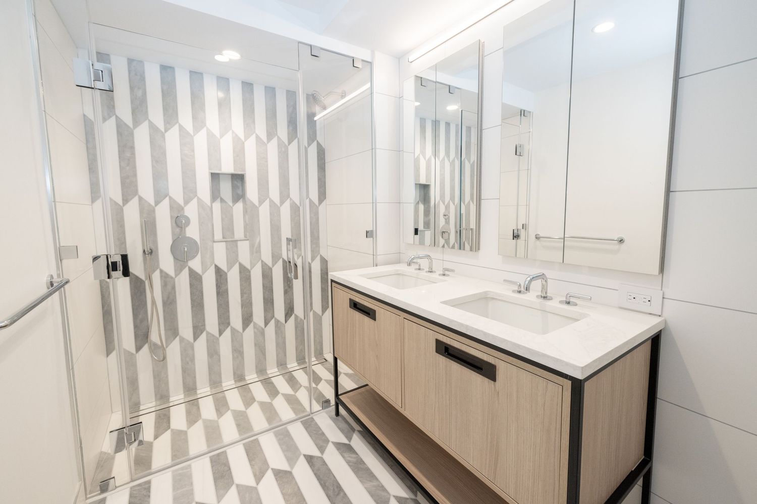 Modern bathroom with geometric patterned tiles, glass shower enclosure, and double vanity with wood cabinets.