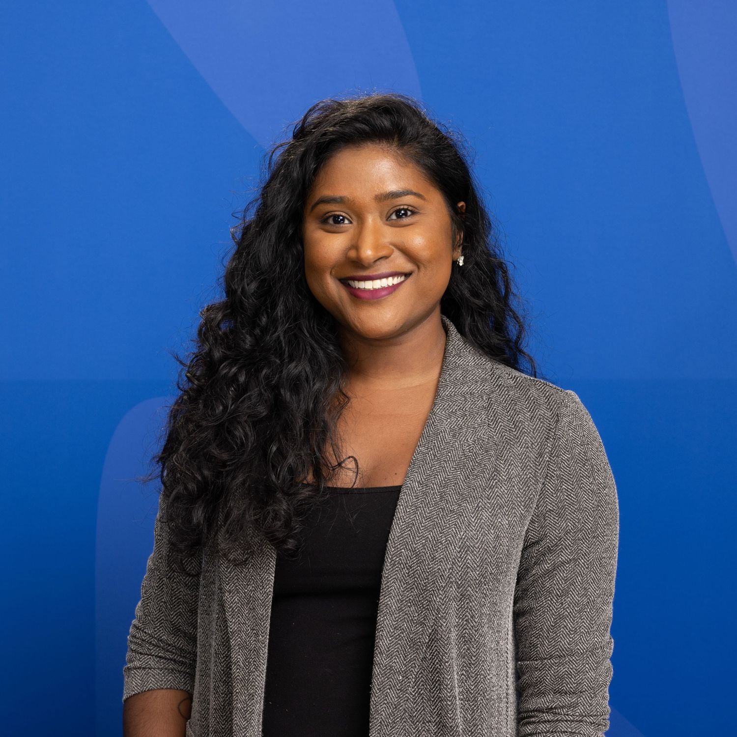 Smiling woman with curly hair in gray cardigan against blue background.
