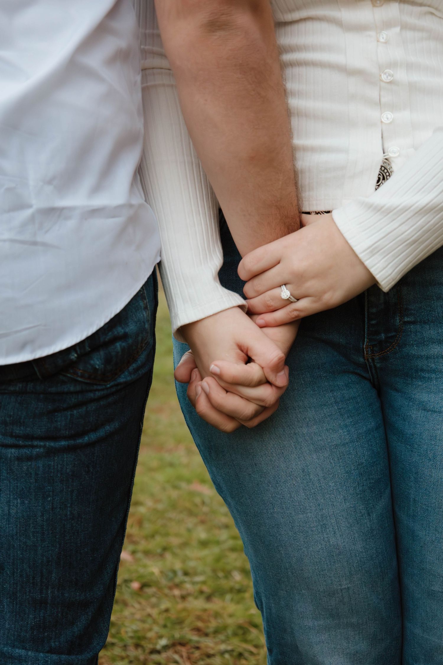 Close-up shot of intertwined hands against denim and white clothing.