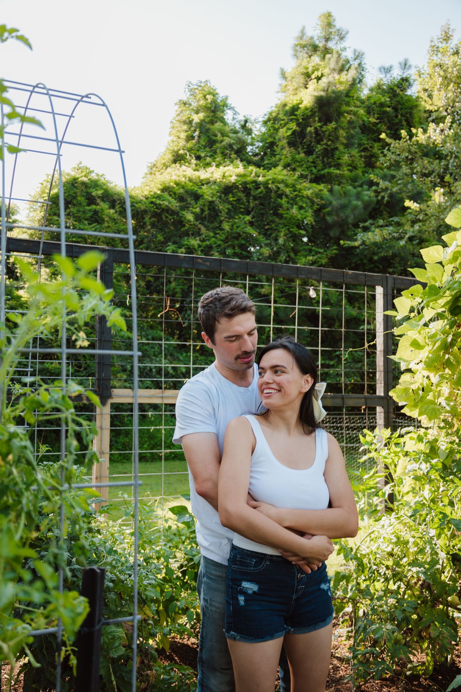 Couple sharing tender moment by garden trellis surrounded by lush greenery.