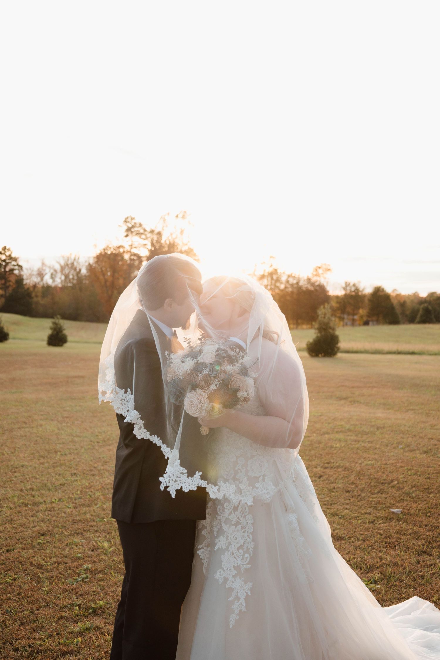 A couple shares an intimate moment in a sunlit field during their wedding.