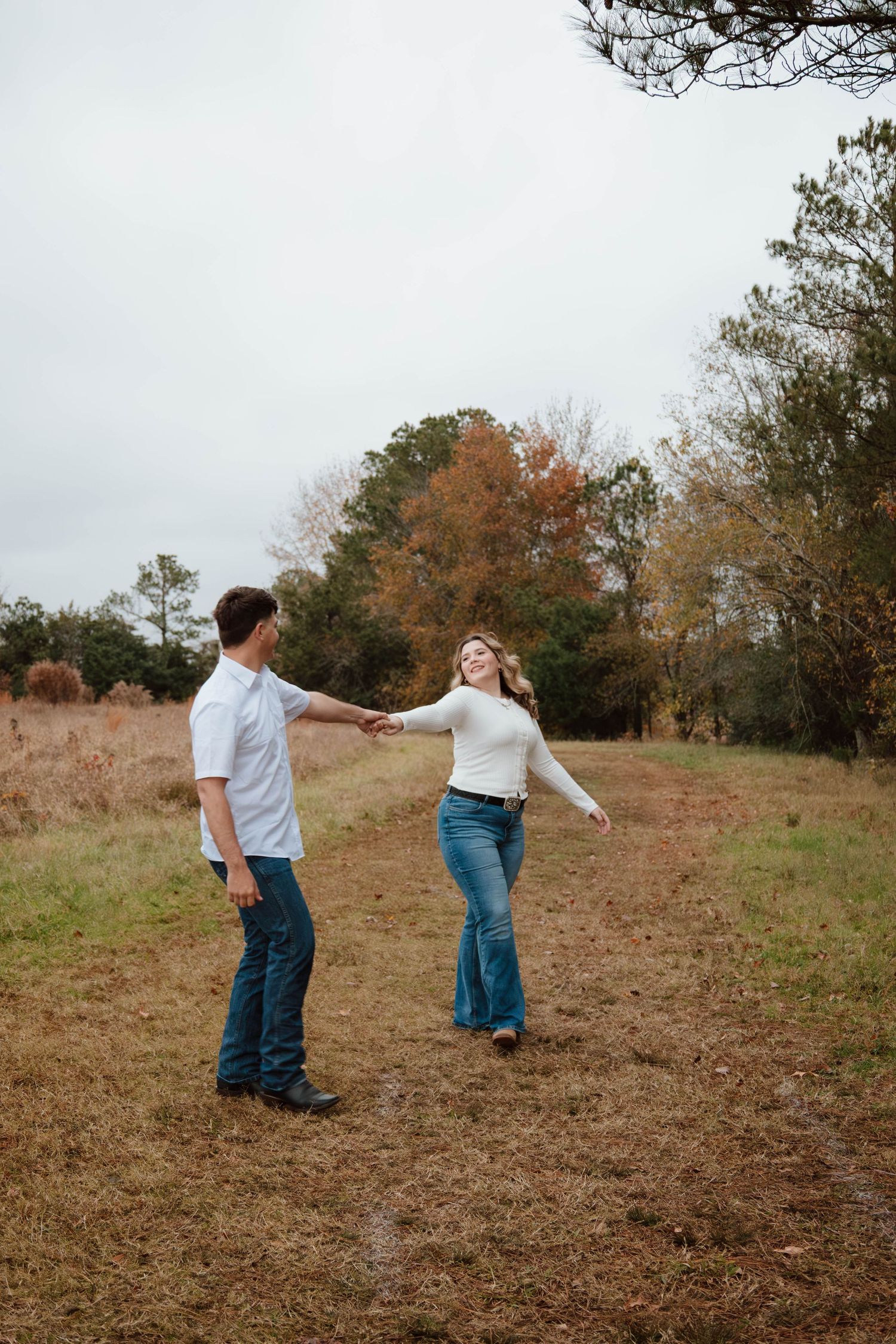 A couple dances playfully in a rustic field during autumn.