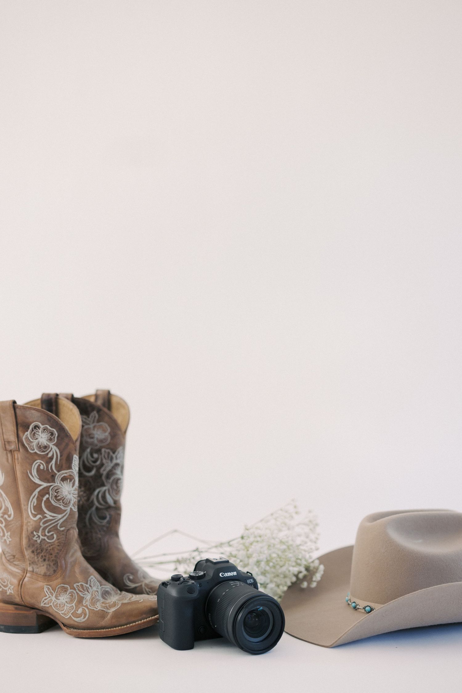 Styled photography flatlay with cowboy boots, DSLR camera and western hat on white background.