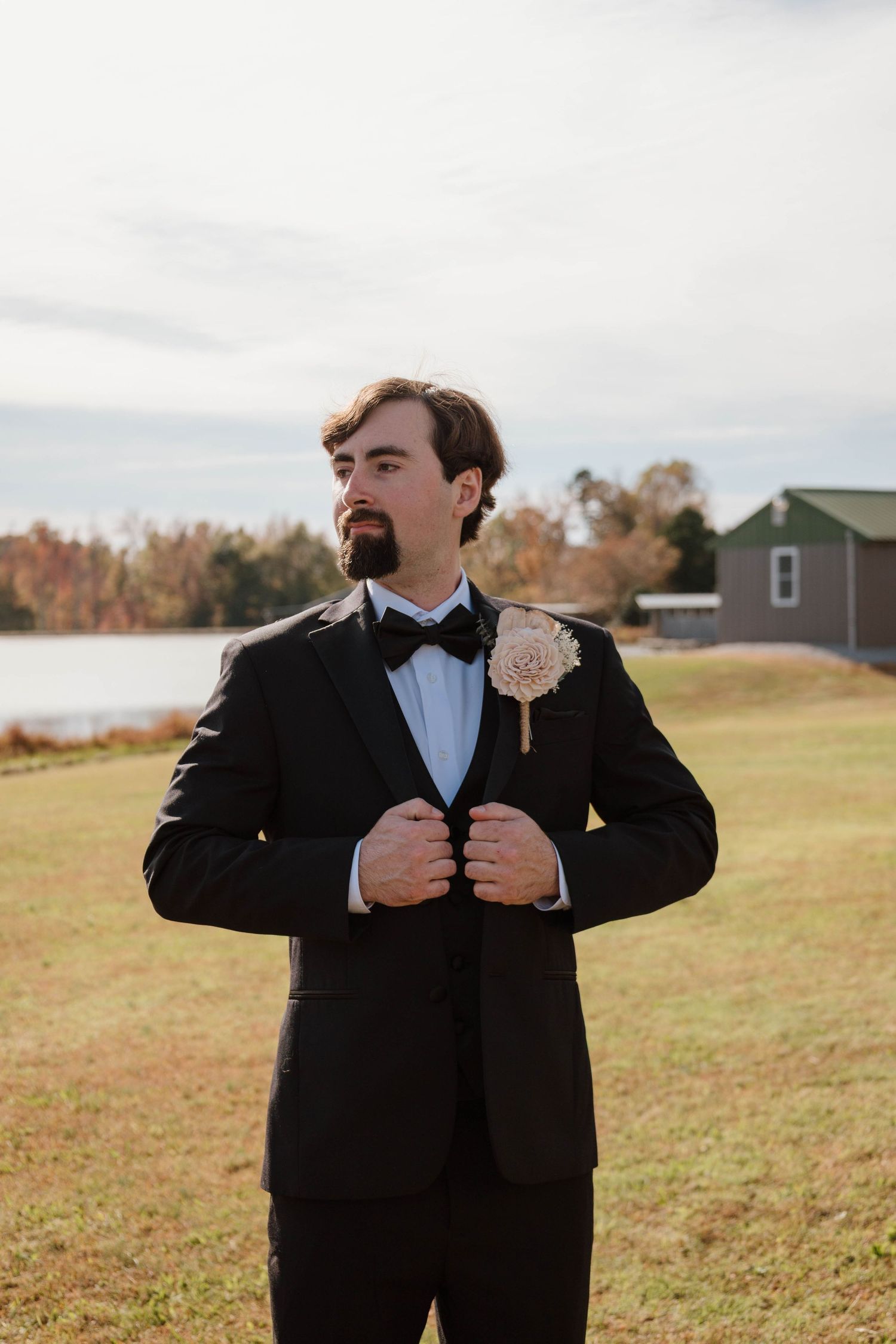 A groom adjusts his formal black tuxedo outdoors on a fall day.