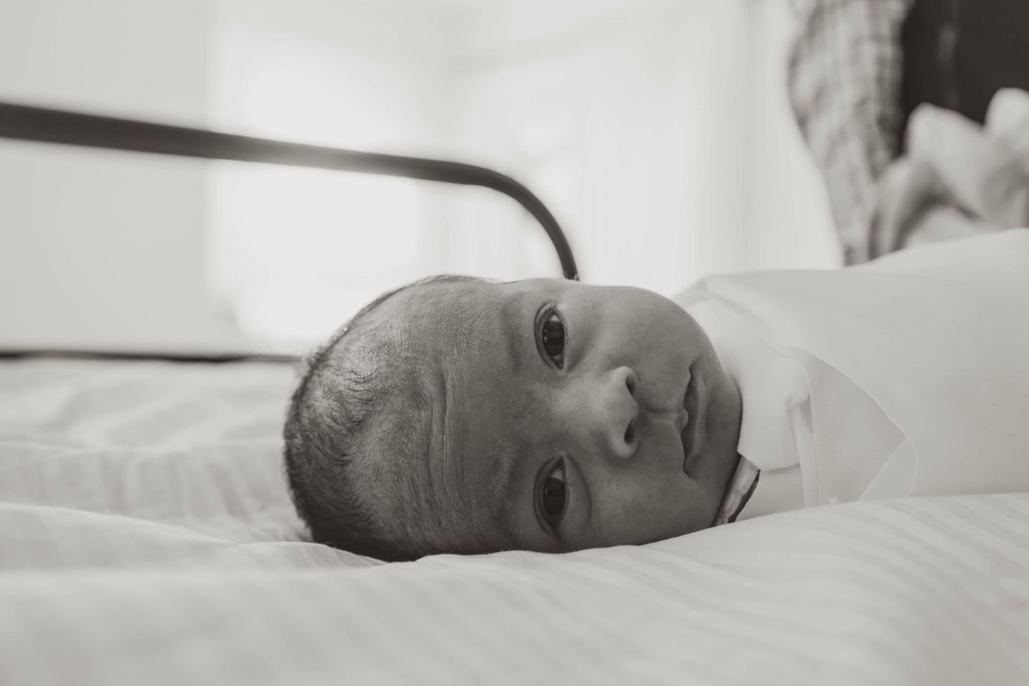Close-up black and white portrait of a newborn baby resting on white bedding.