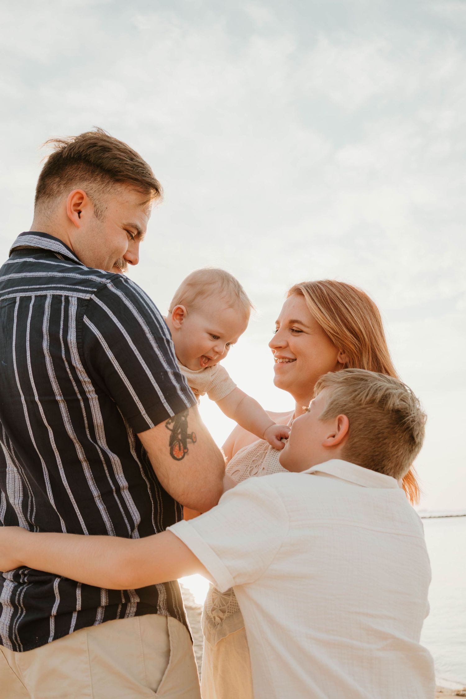 Happy family with baby and young boy enjoying a sunny beach day together, smiling and bonding outdoors.