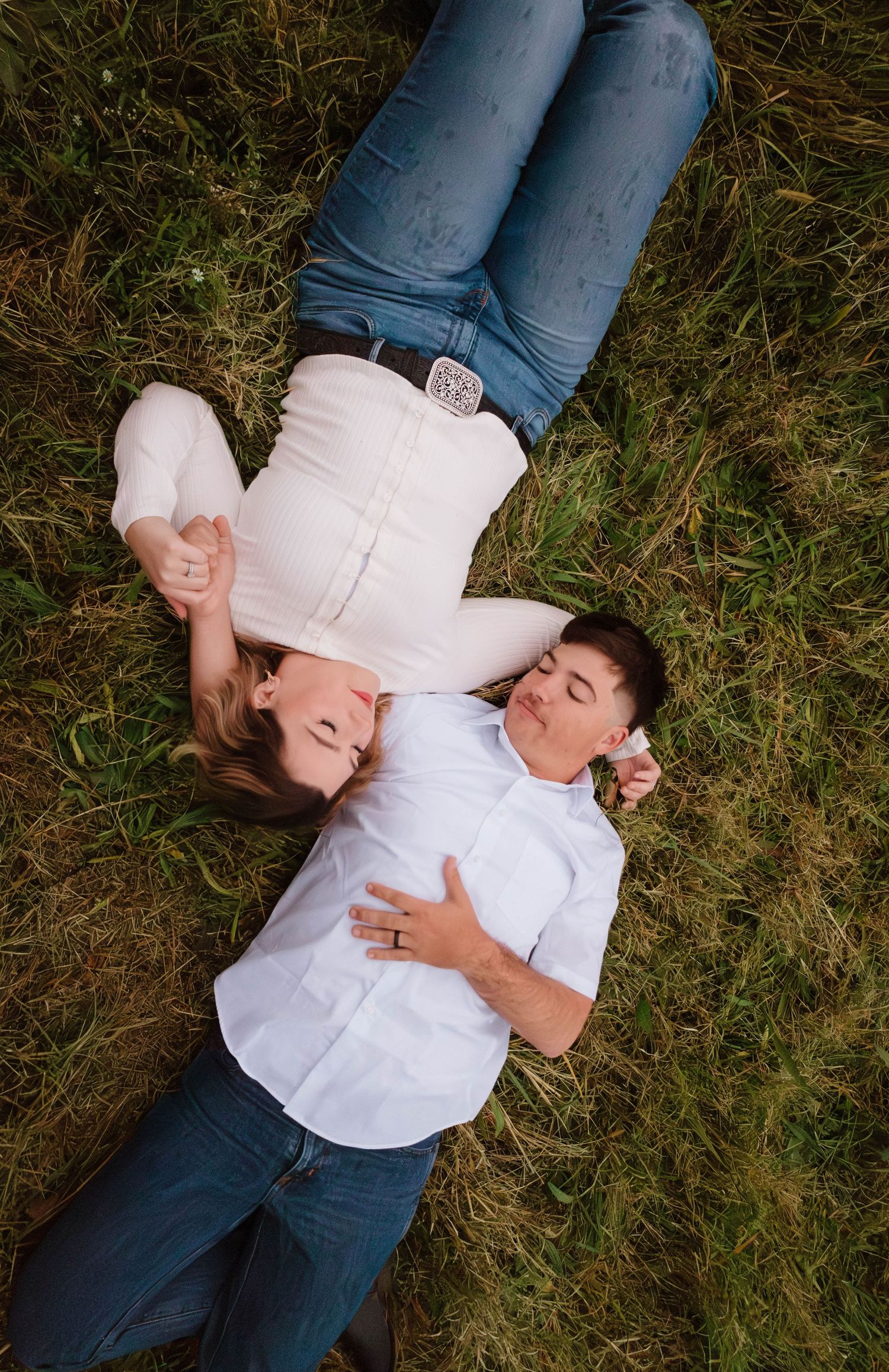 A couple lies together in grass during a romantic outdoor photoshoot.