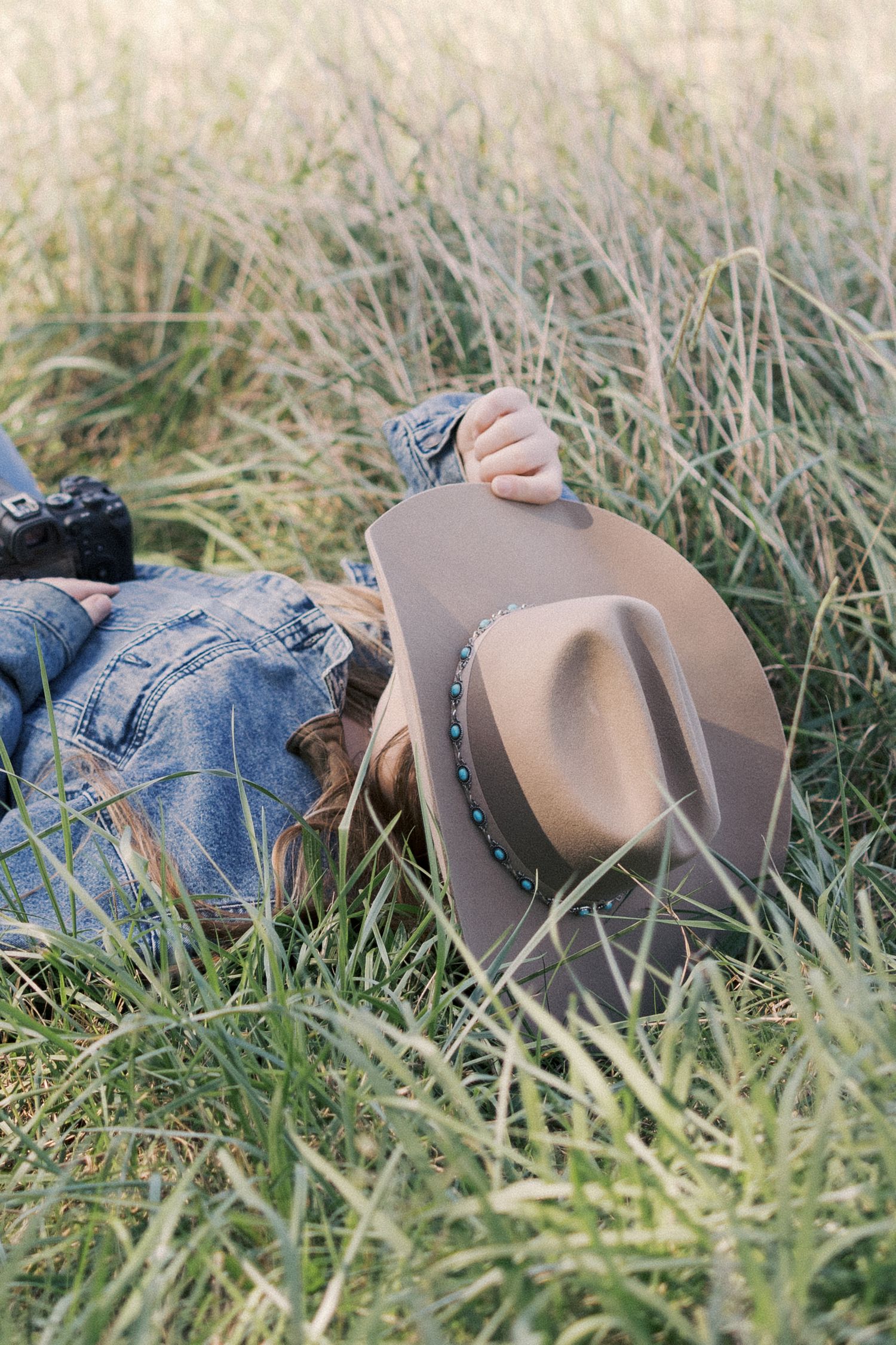 A brown cowboy hat and denim jacket lay in tall grass during a relaxing outdoor moment.