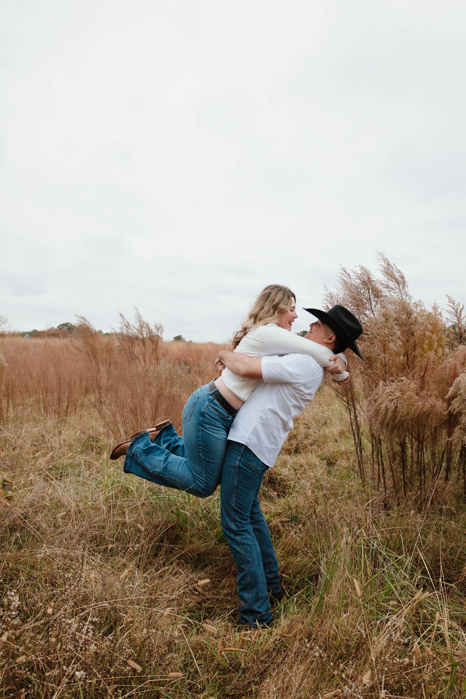 A playful couple embraces while spinning in a grassy field.