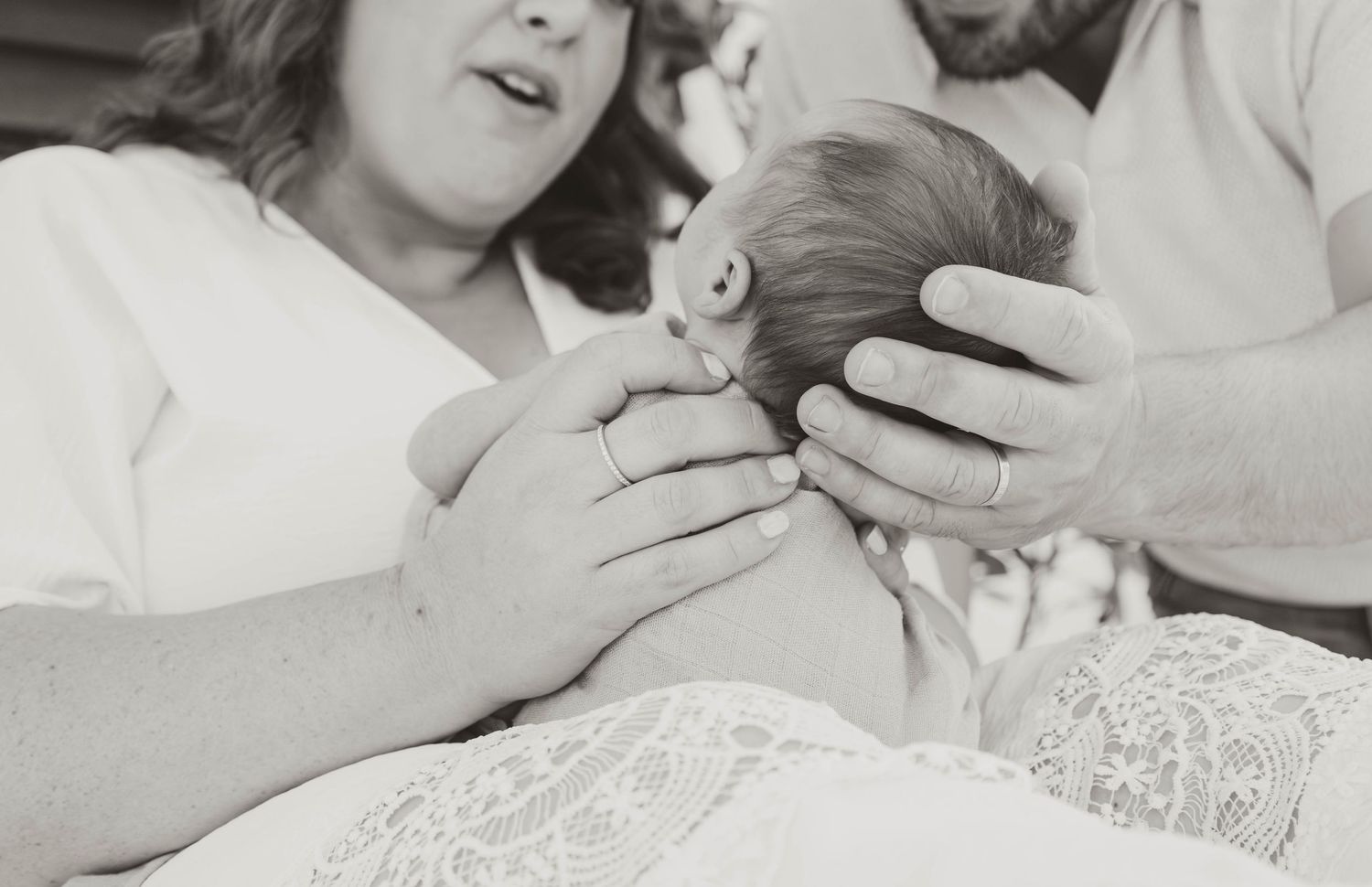 Black and white photo of new parents holding their newborn baby in a hospital room after birth.