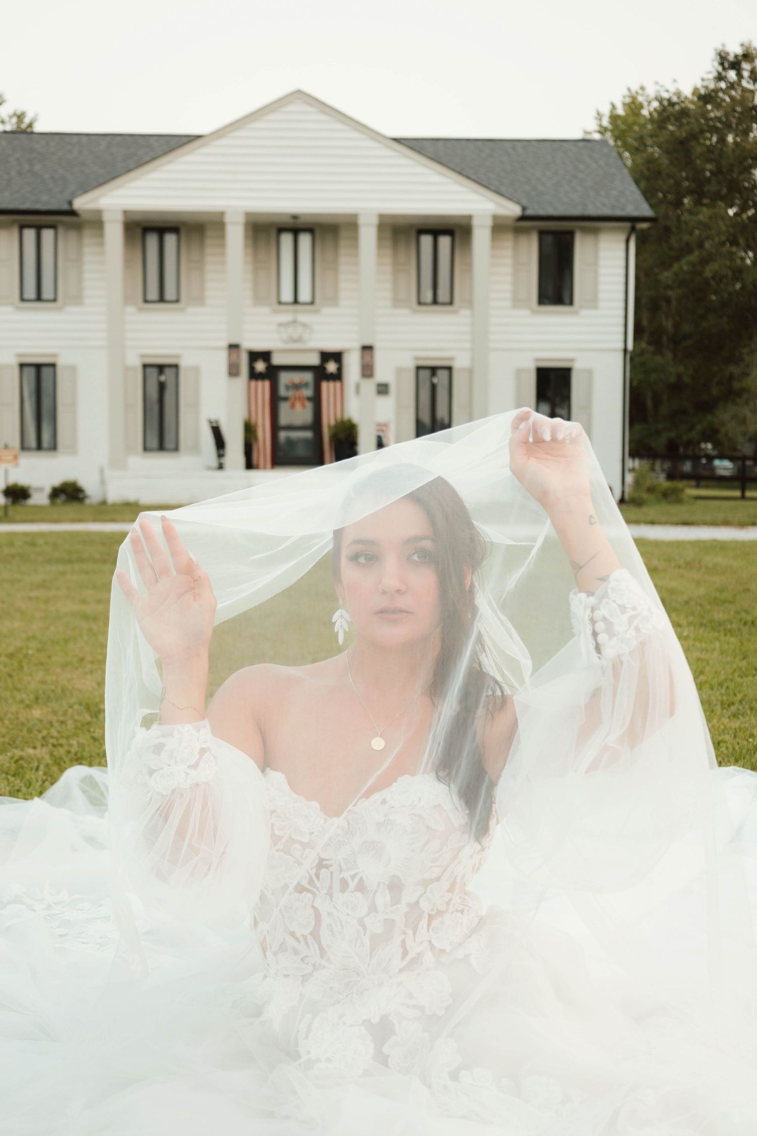 A bride playfully lifts her delicate white veil against a white building backdrop.