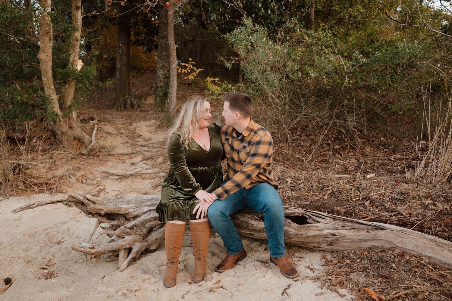 A couple sits together on a fallen tree trunk in a wooded outdoor setting.