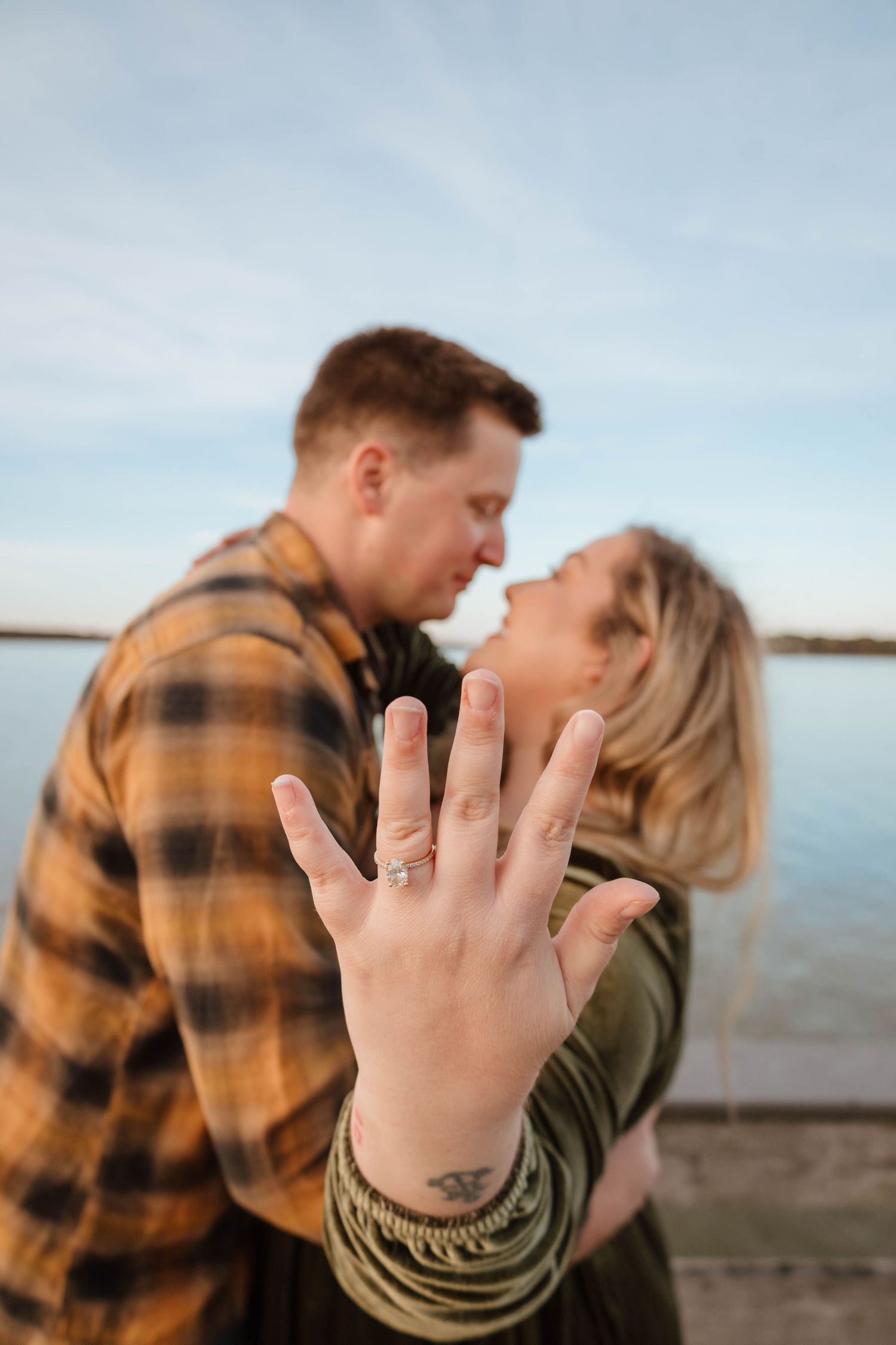 Hand displaying engagement ring on wooden dock by the water.