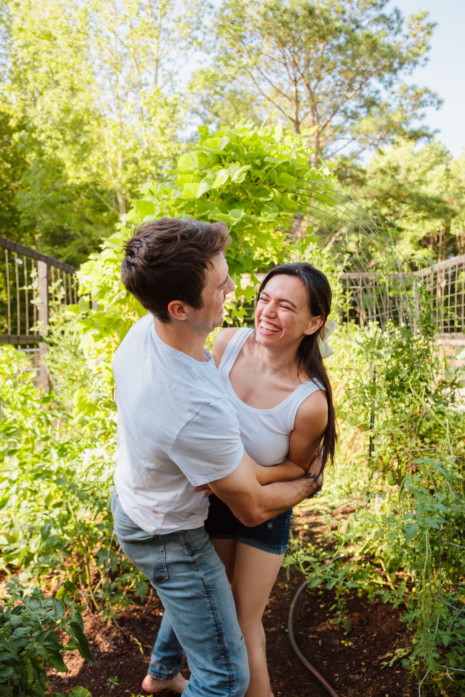 Couple embracing and laughing together in a lush garden setting on a sunny day.