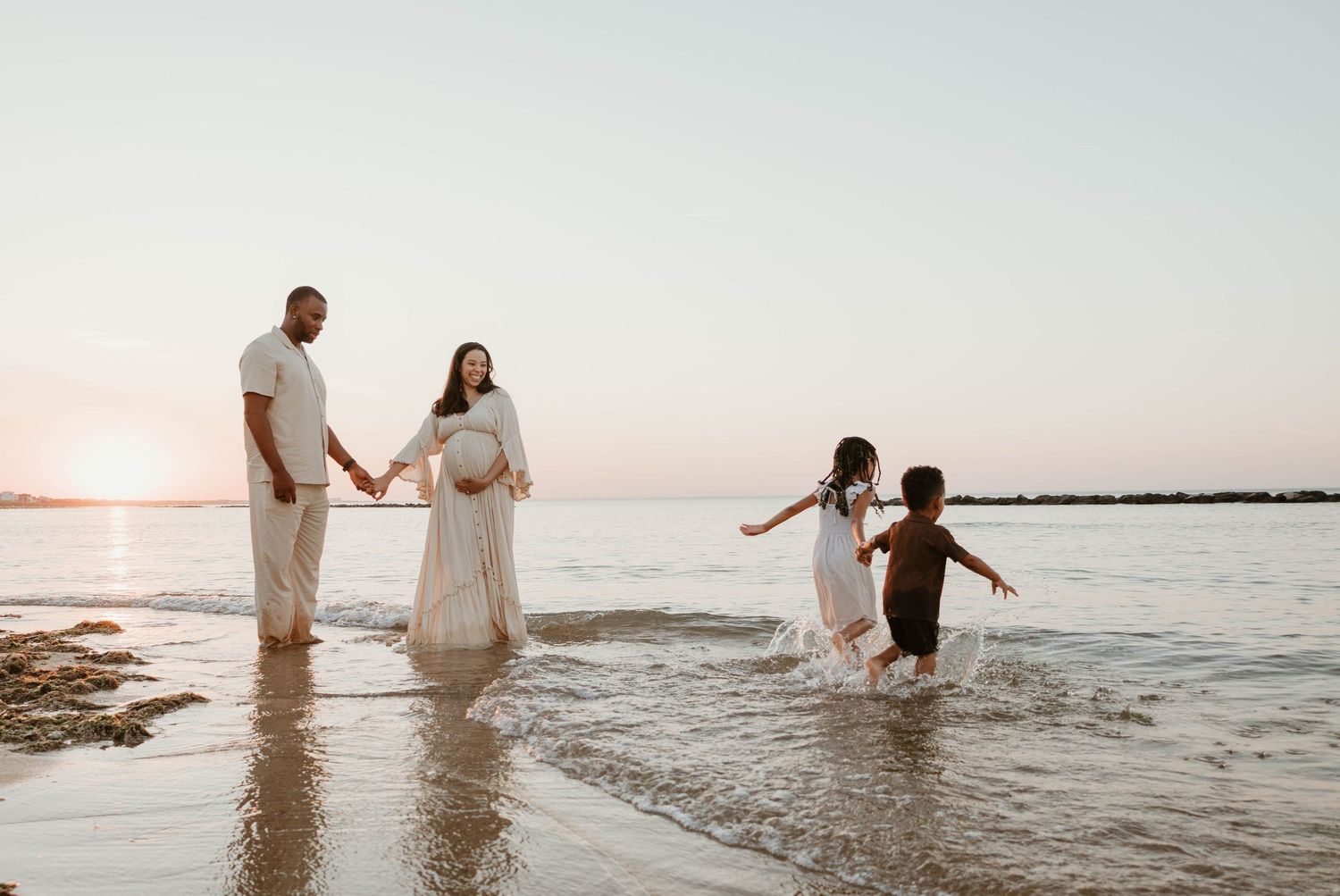Pregnant woman and family walking on beach at sunset, children playing in waves.