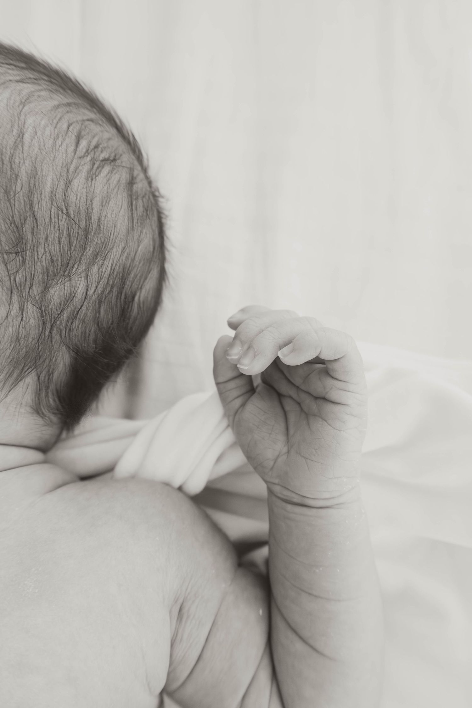 Black and white close-up of a newborn baby's head and tiny hand, capturing delicate details of new life.
