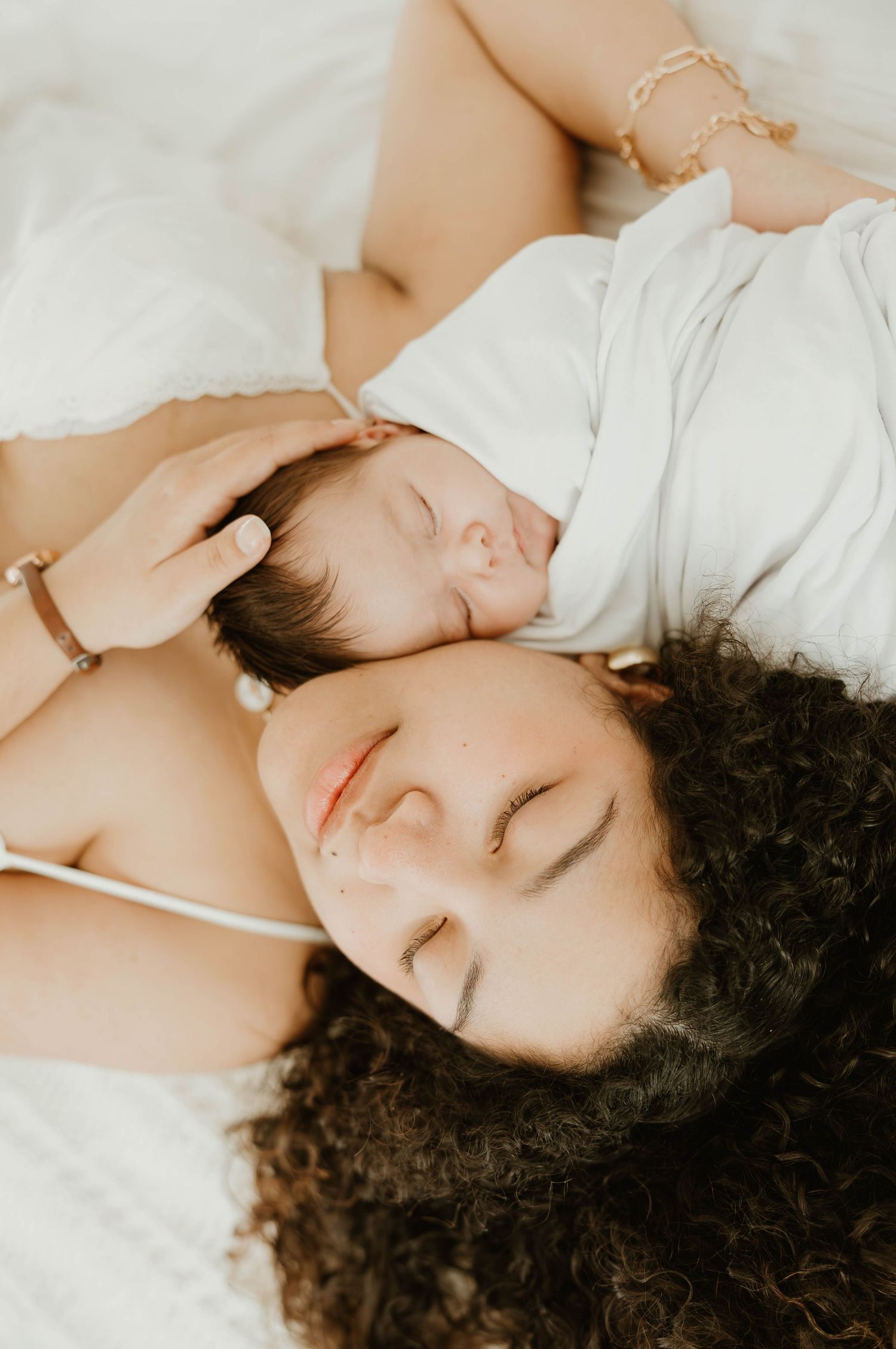 Mother and newborn baby lying together on white bedding, sharing a peaceful and tender moment.