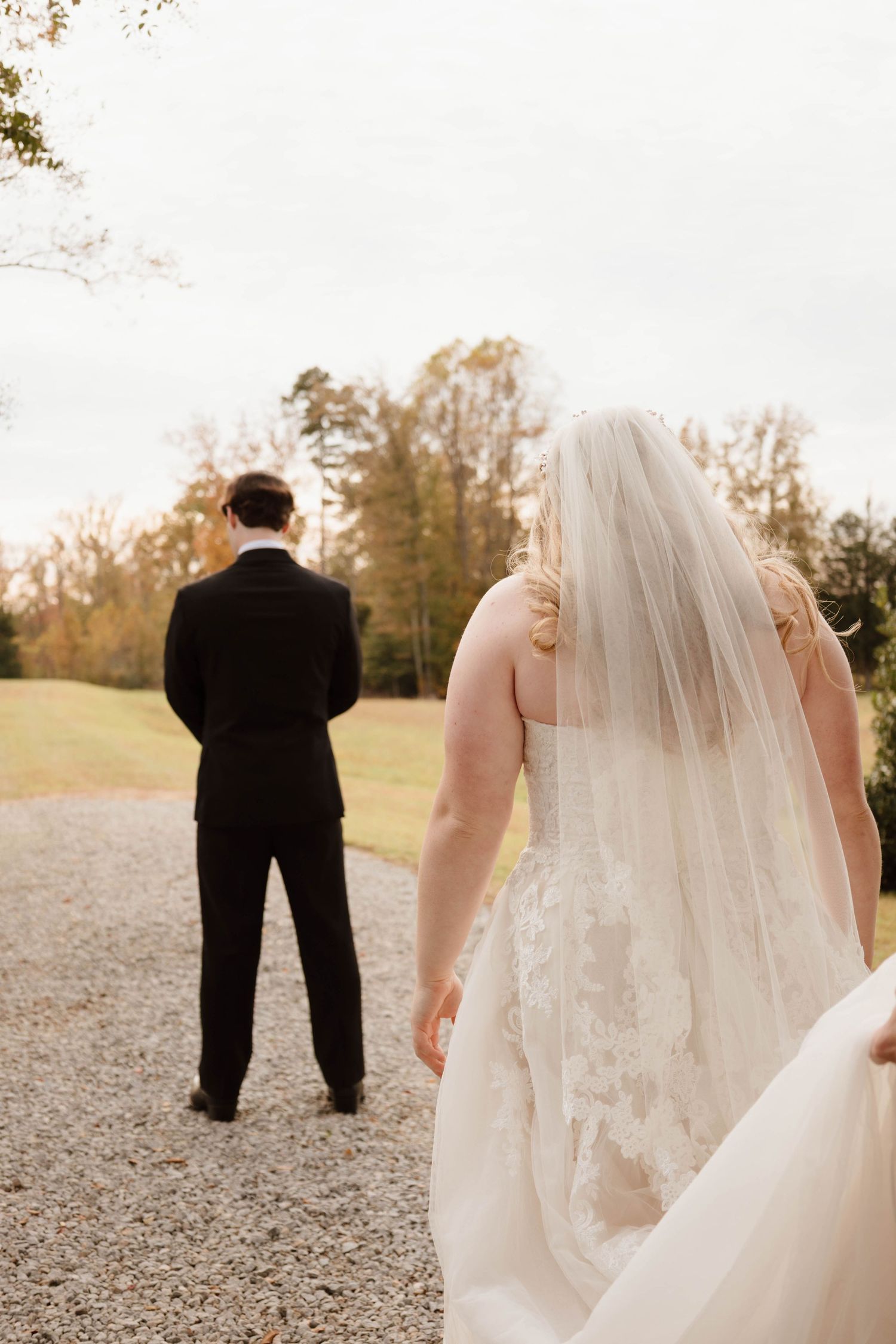 First look wedding moment captured from behind on a gravel path in autumn.