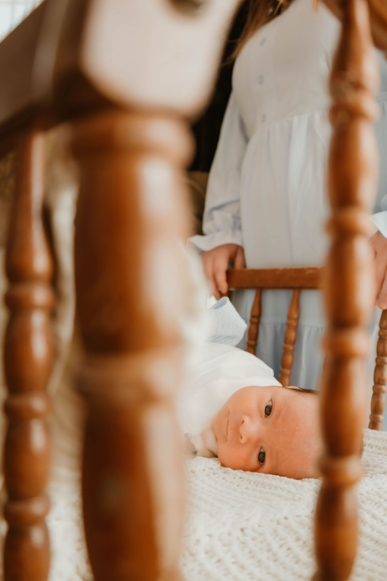 Close-up view through wooden crib slats showing a baby lying on white bedding.