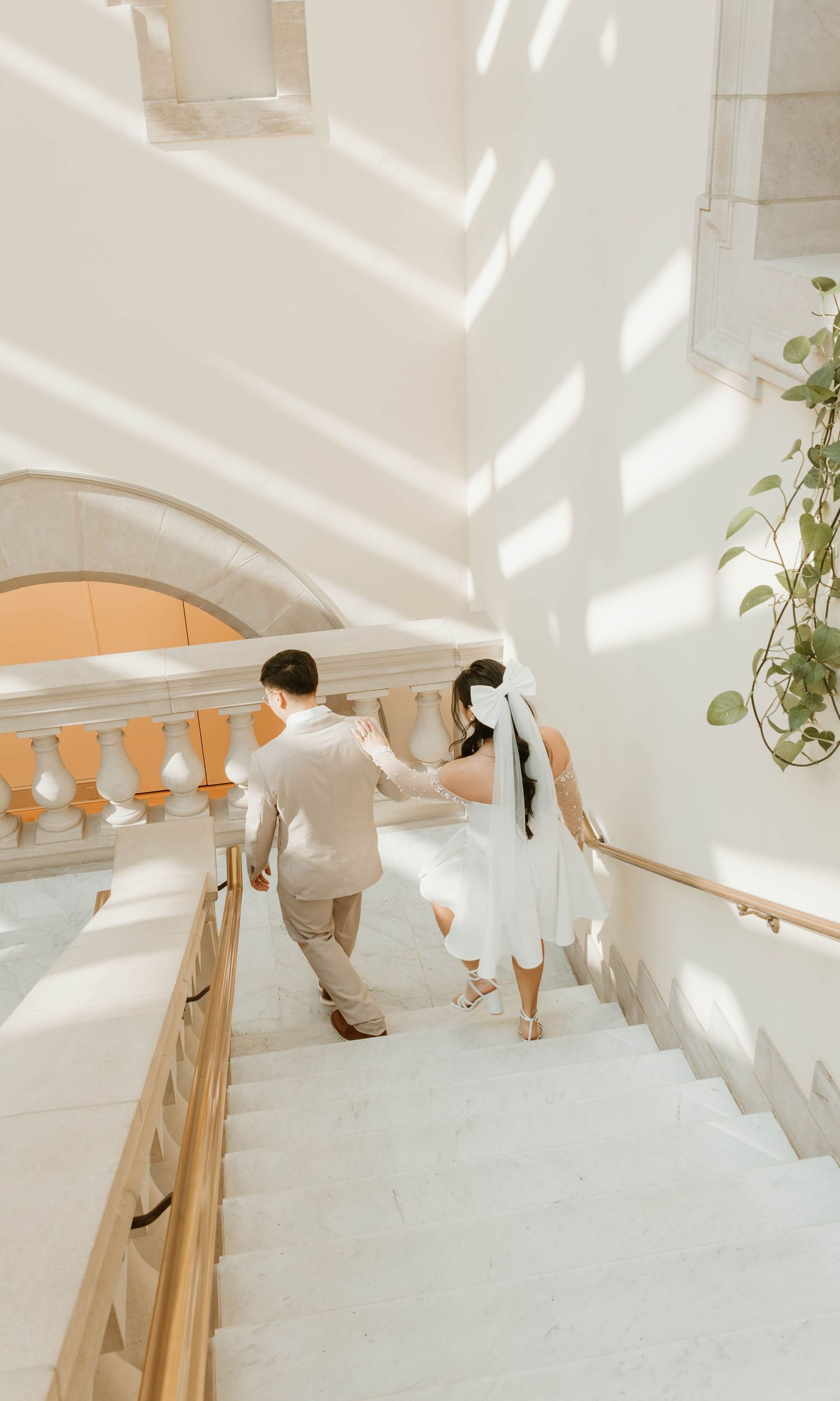 A bride and groom walking up a grand staircase with ornate white balustrades.
