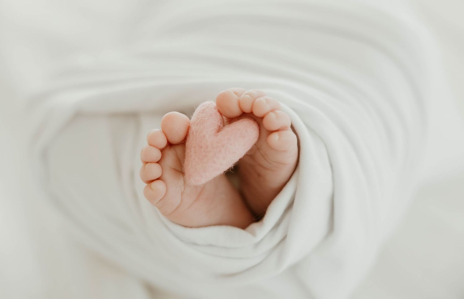Newborn baby feet wrapped in a soft white blanket with toes forming a sweet heart shape, perfect newborn photography.