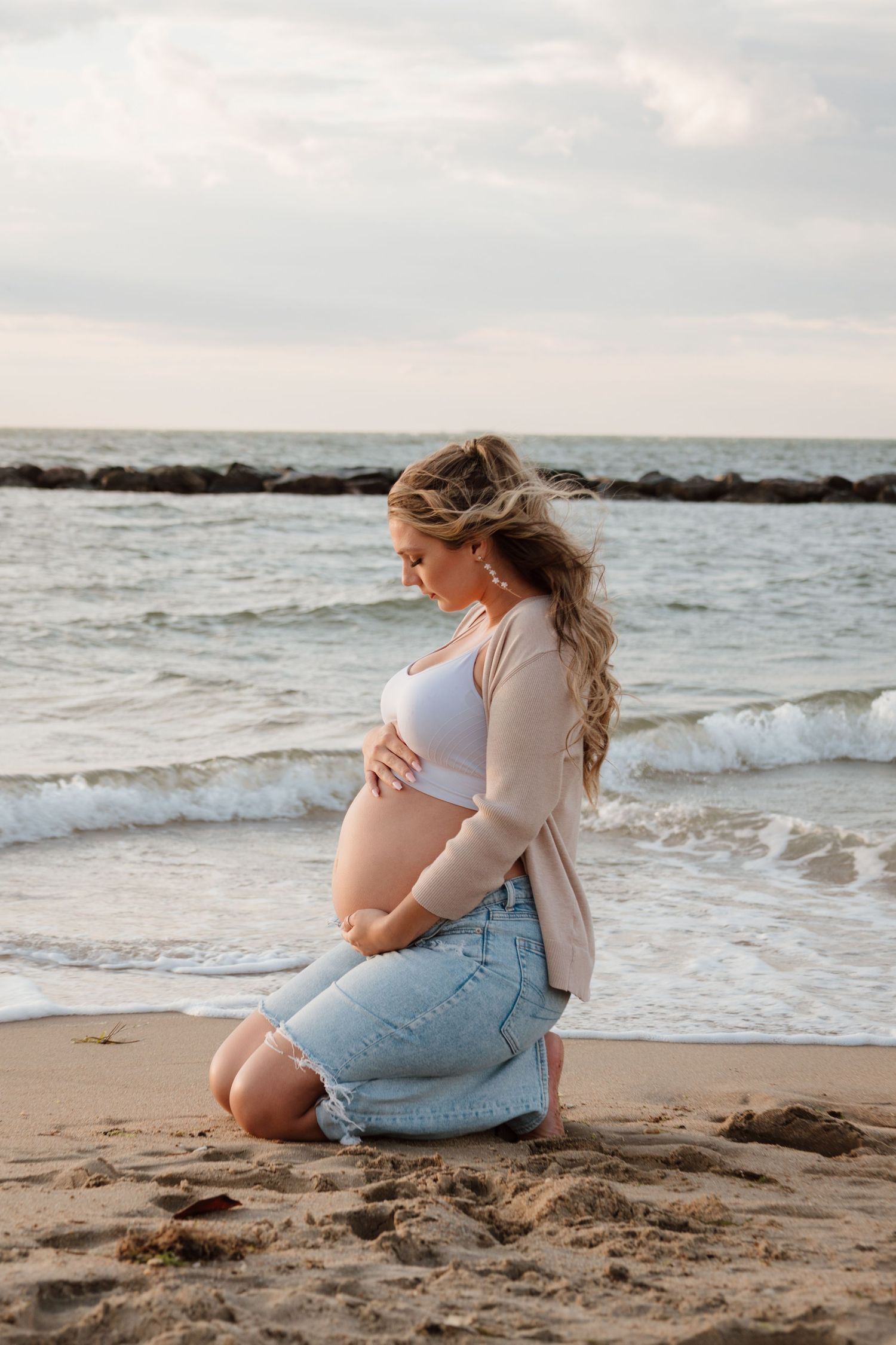 Maternity photos at sunset on a beach with waves crashing against rocky shore in background.