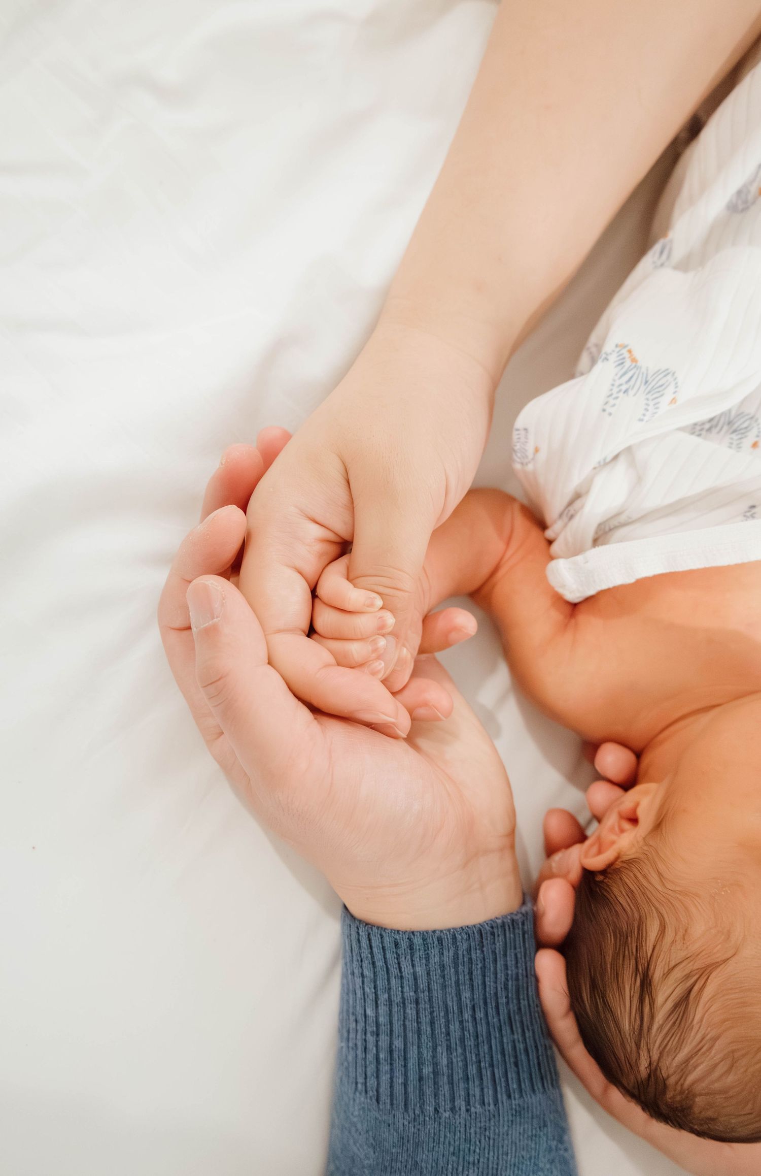 A tender moment showing adult hands gently cradling a baby's tiny hand against white bedding.
