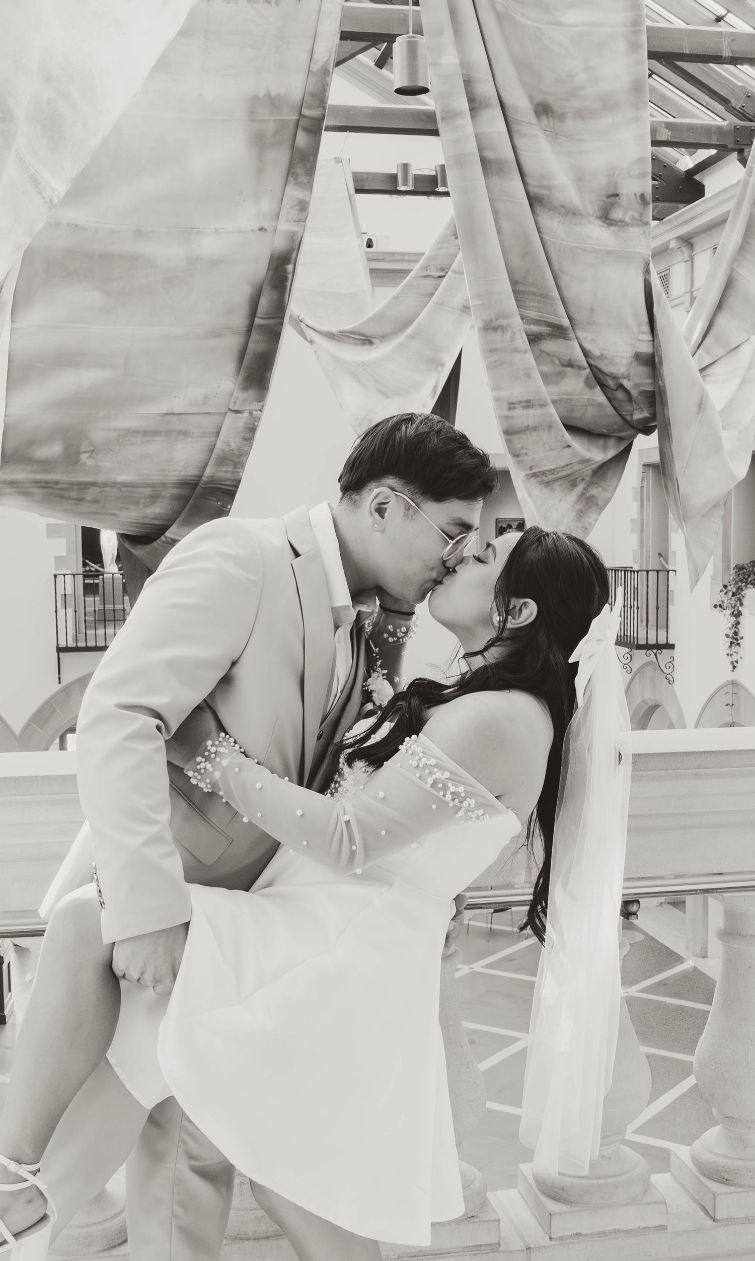 A black and white image of a bride and groom embracing and kissing in front of a decorative backdrop.