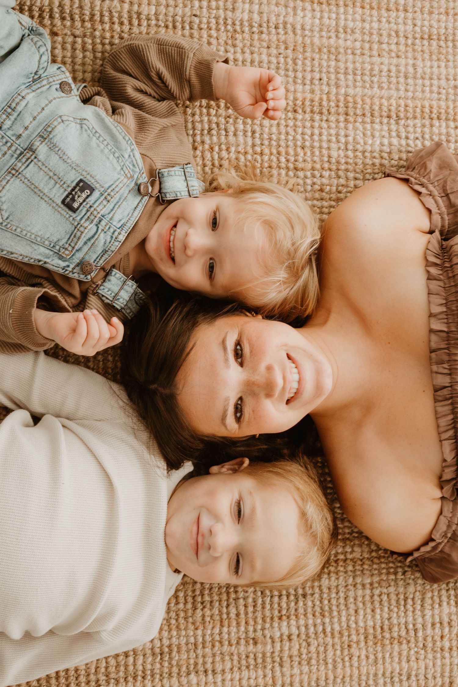 Overhead view of a family laying together on a textured beige carpet with warm lighting and soft expressions.