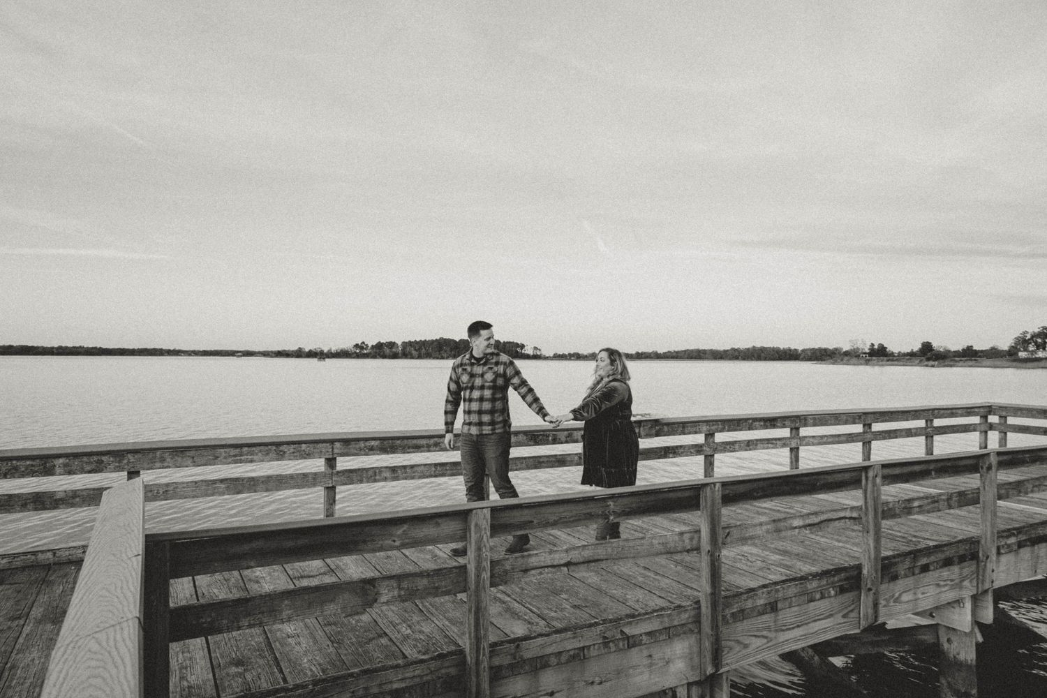 Long wooden boardwalk stretches across a serene waterfront landscape.