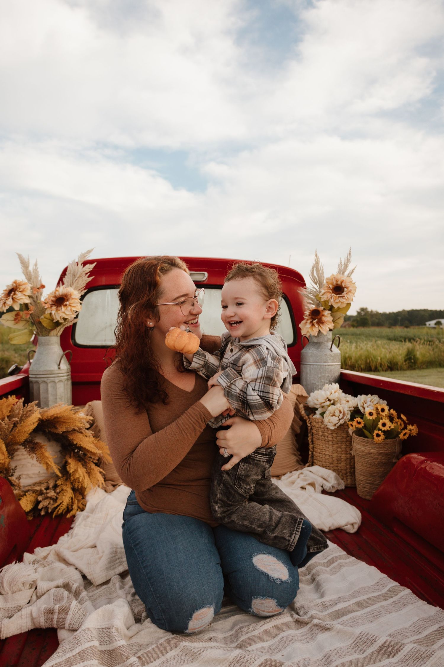 Playful mother and child moments captured in a decorated red truck bed with autumn decor.