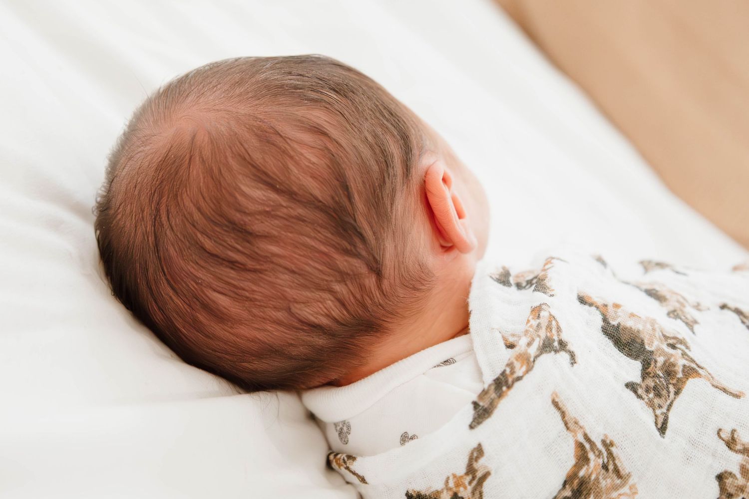 Detail shots of a sleeping newborn baby wrapped in patterned swaddle blanket.