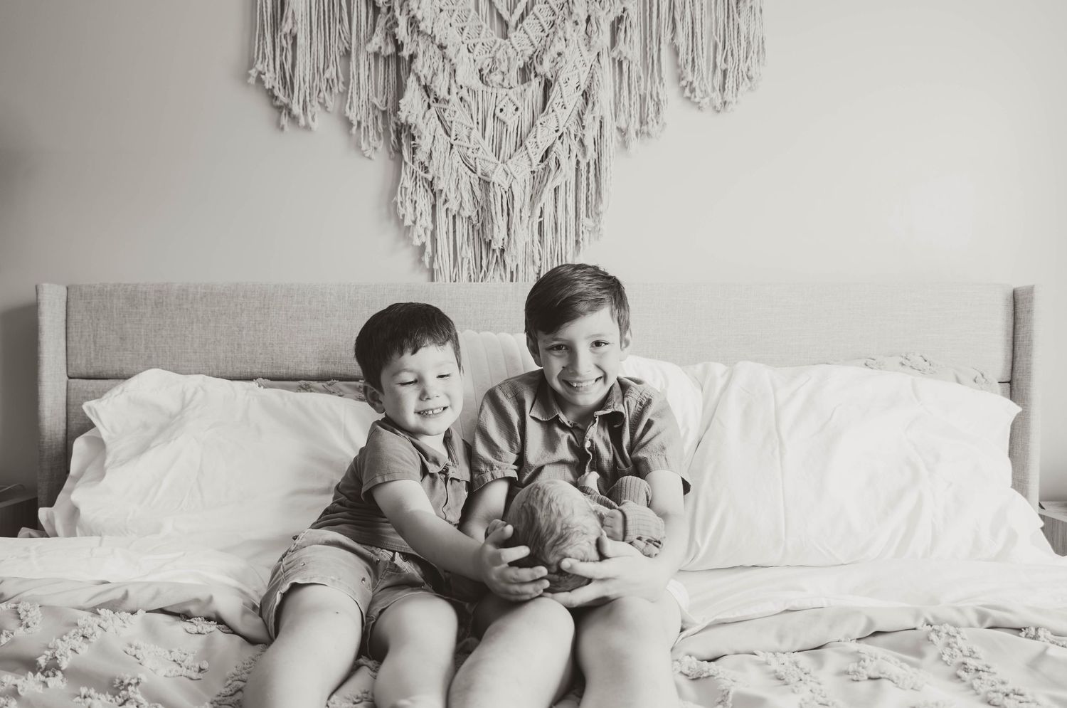 Two young brothers smiling and sitting together on a bed, black and white portrait photo.