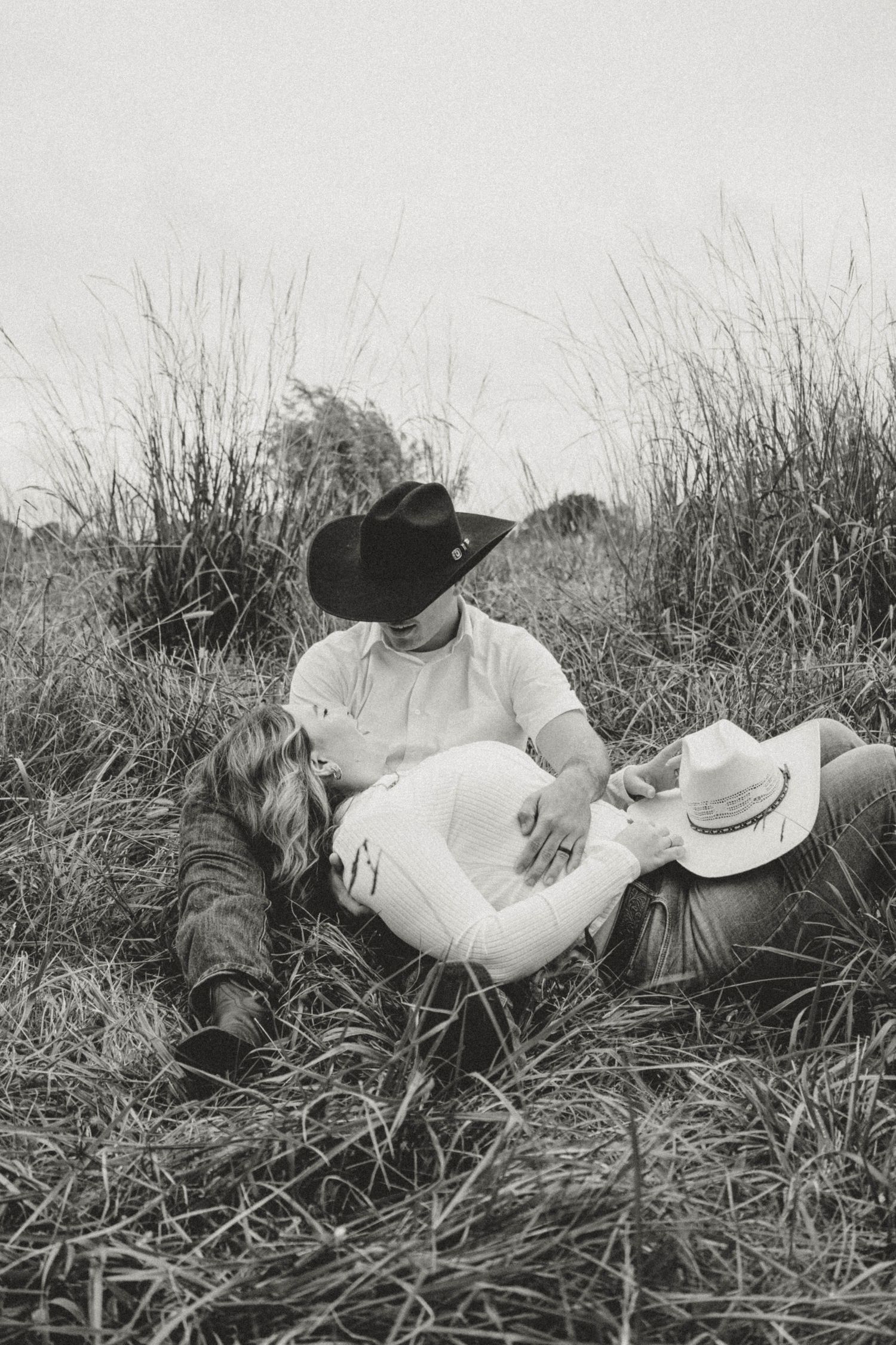 A couple lies together in tall grass during a romantic black and white photo session.