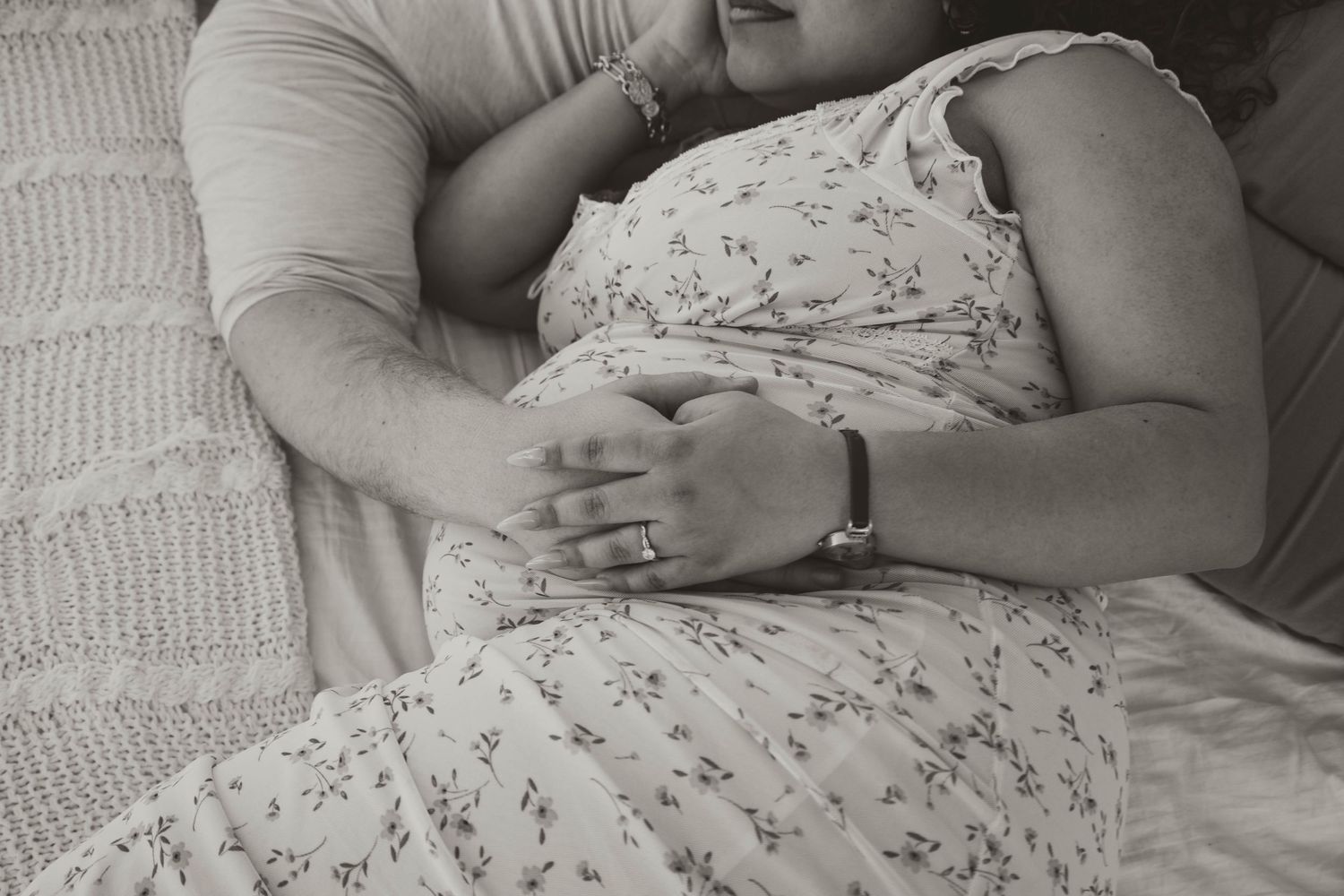 A black and white close-up image of a sleeping baby cuddled in a parent's arms.