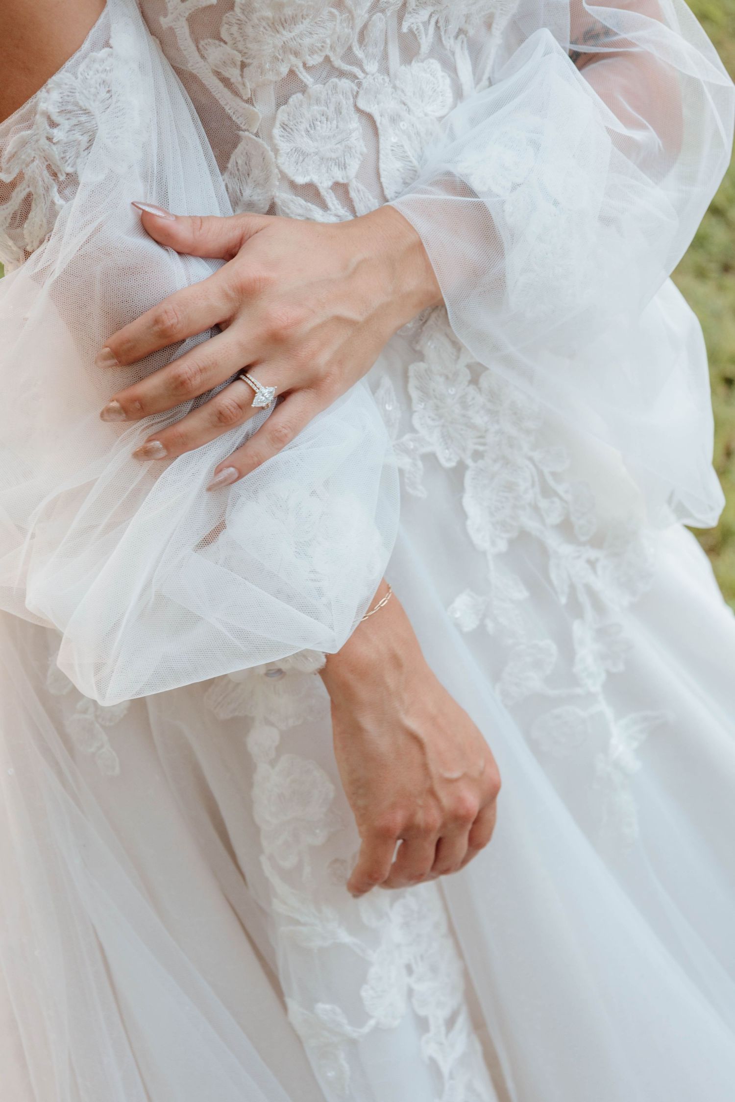 Close-up of an engagement ring and lace details on a white wedding dress.