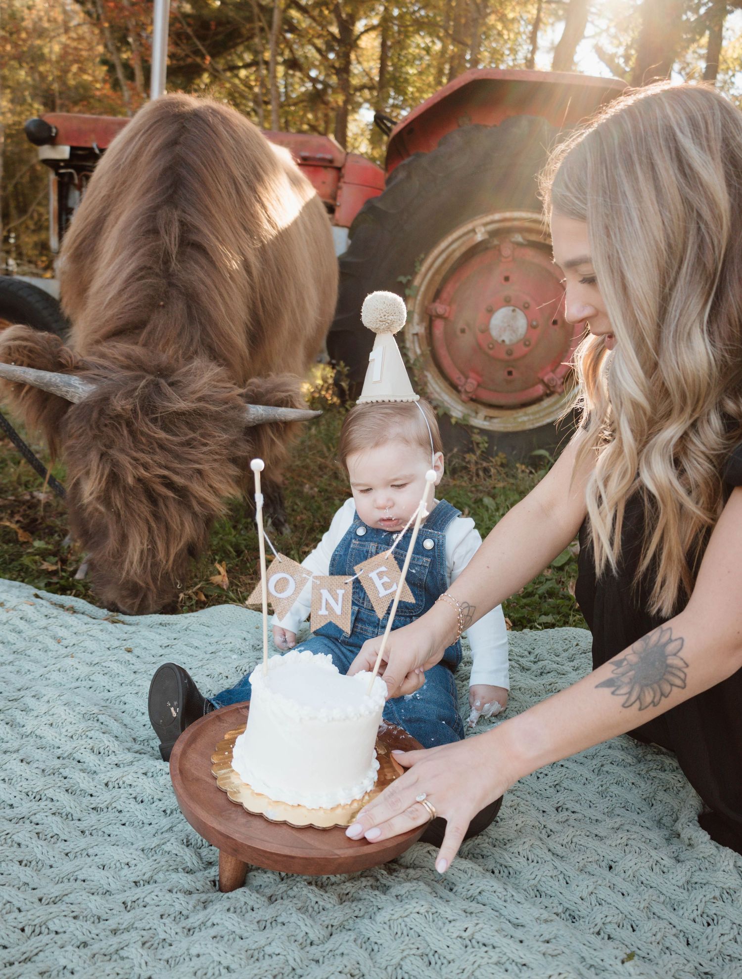 Cake smash photo session with baby and family outdoors near vintage farm equipment.