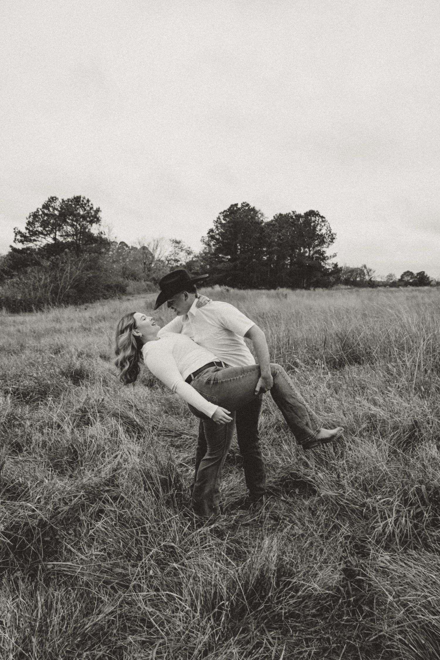 Black and white photo of romantic dip pose in rustic field setting.