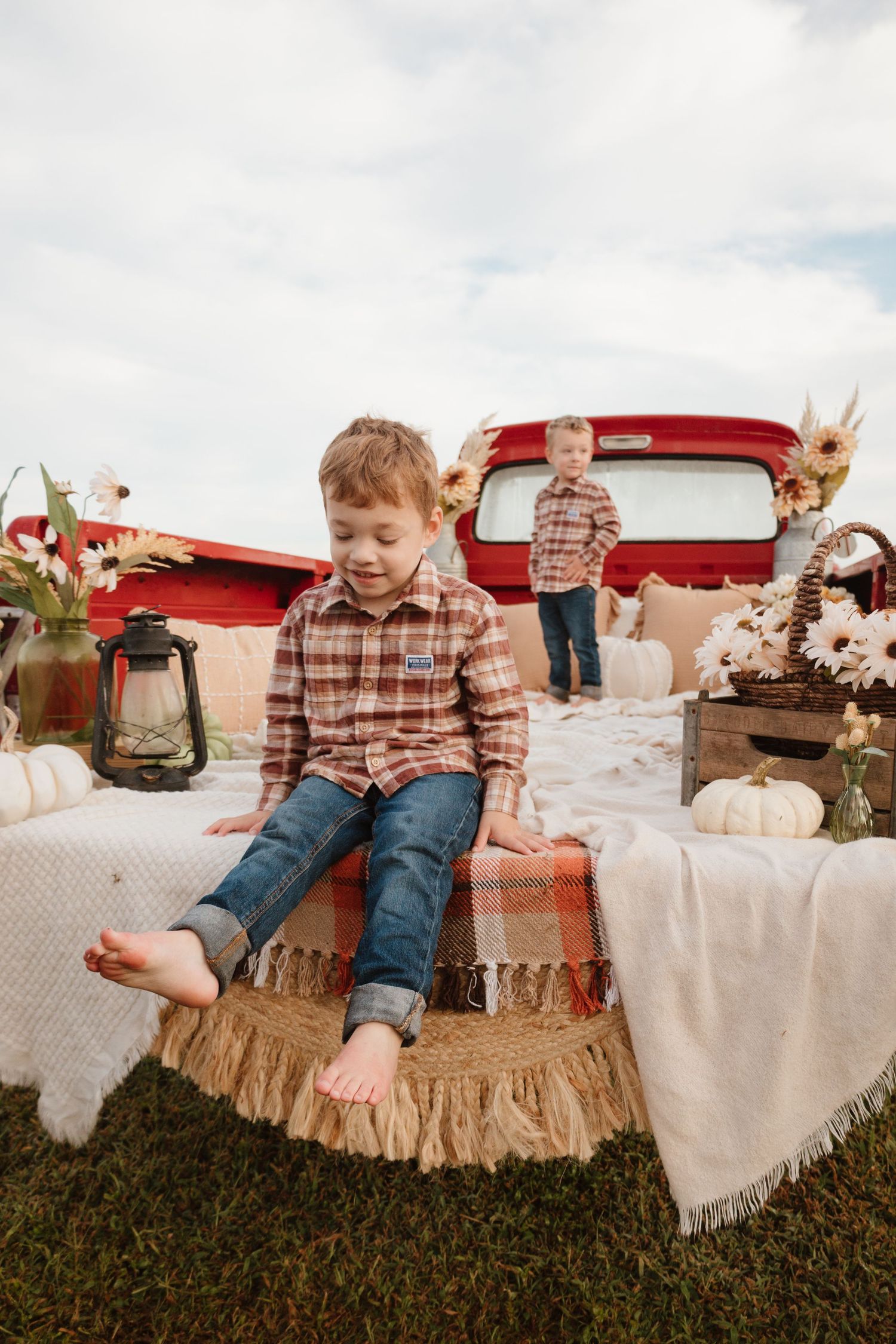 Child playing and posing in vintage red truck bed decorated with rustic blankets and autumn decor.