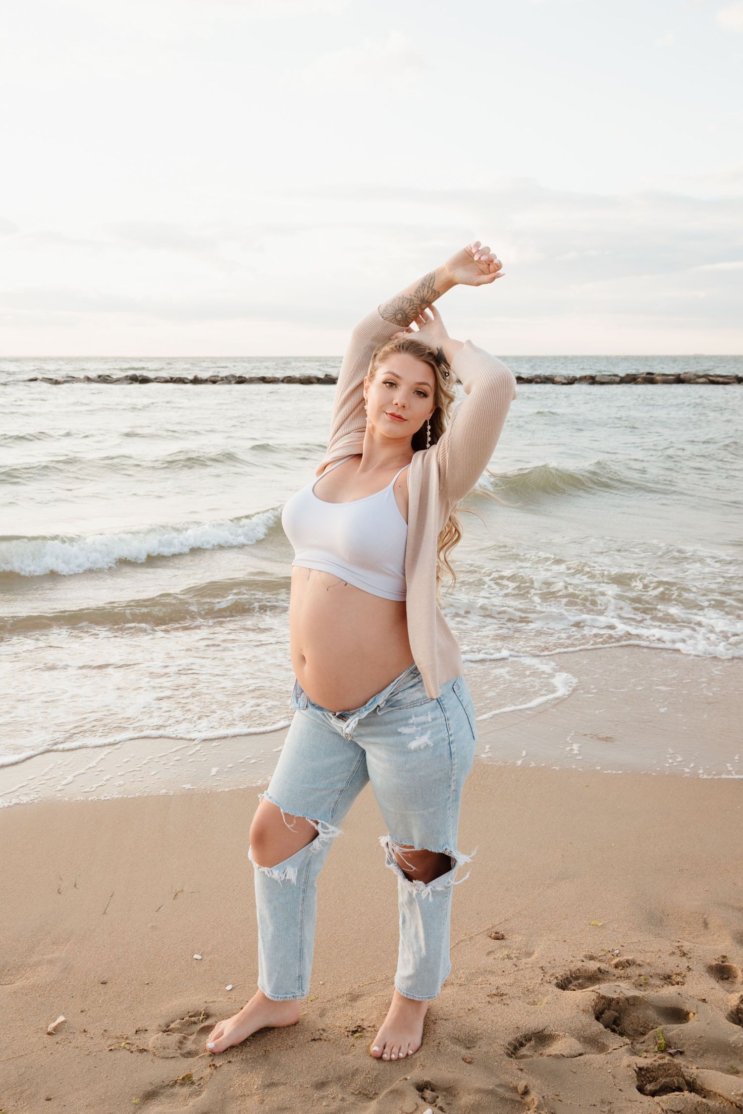 Woman in casual beachwear posing playfully on the sand near ocean waves.