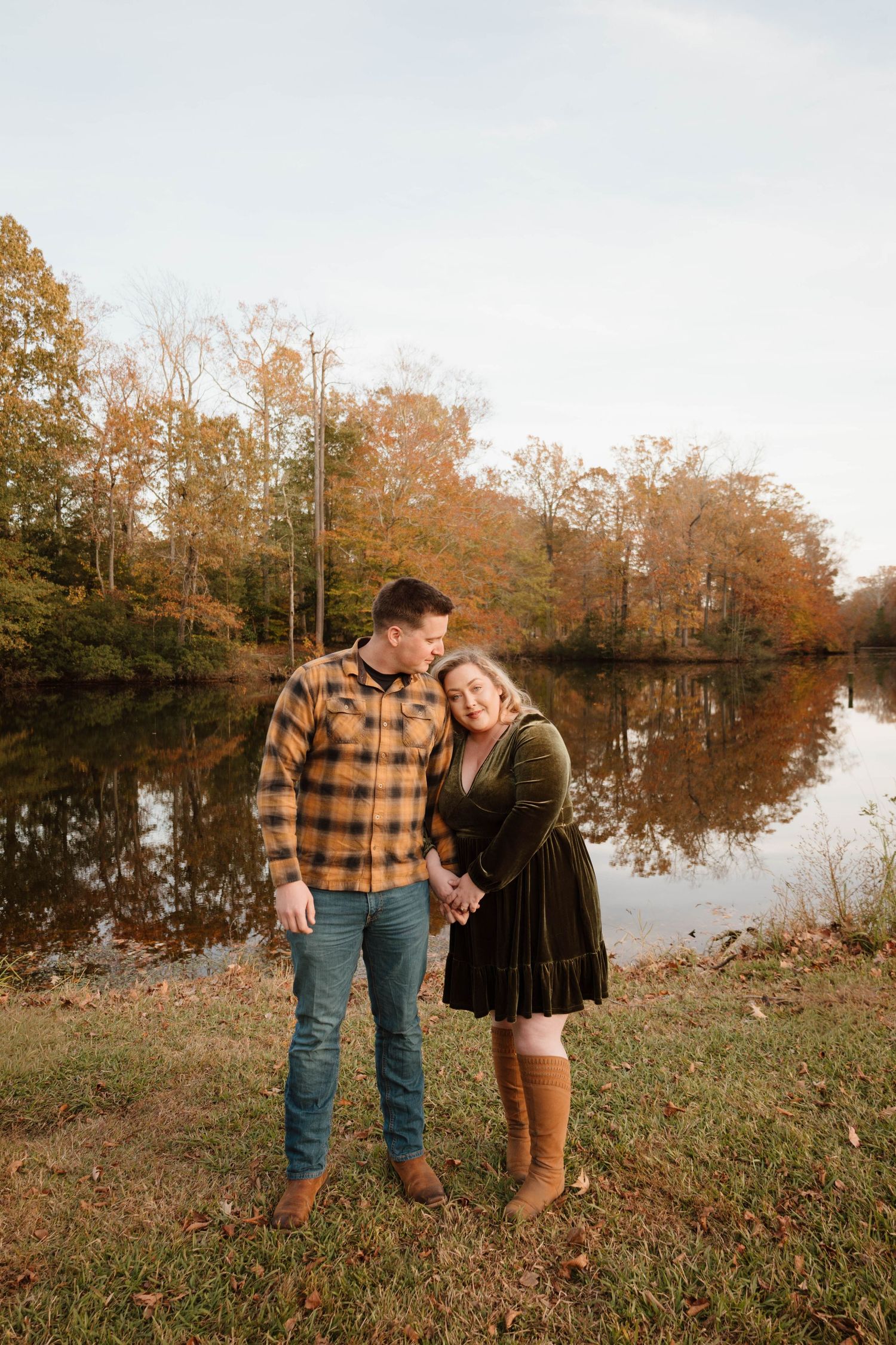 Romantic autumn photoshoot by a lake with fall foliage in the background.