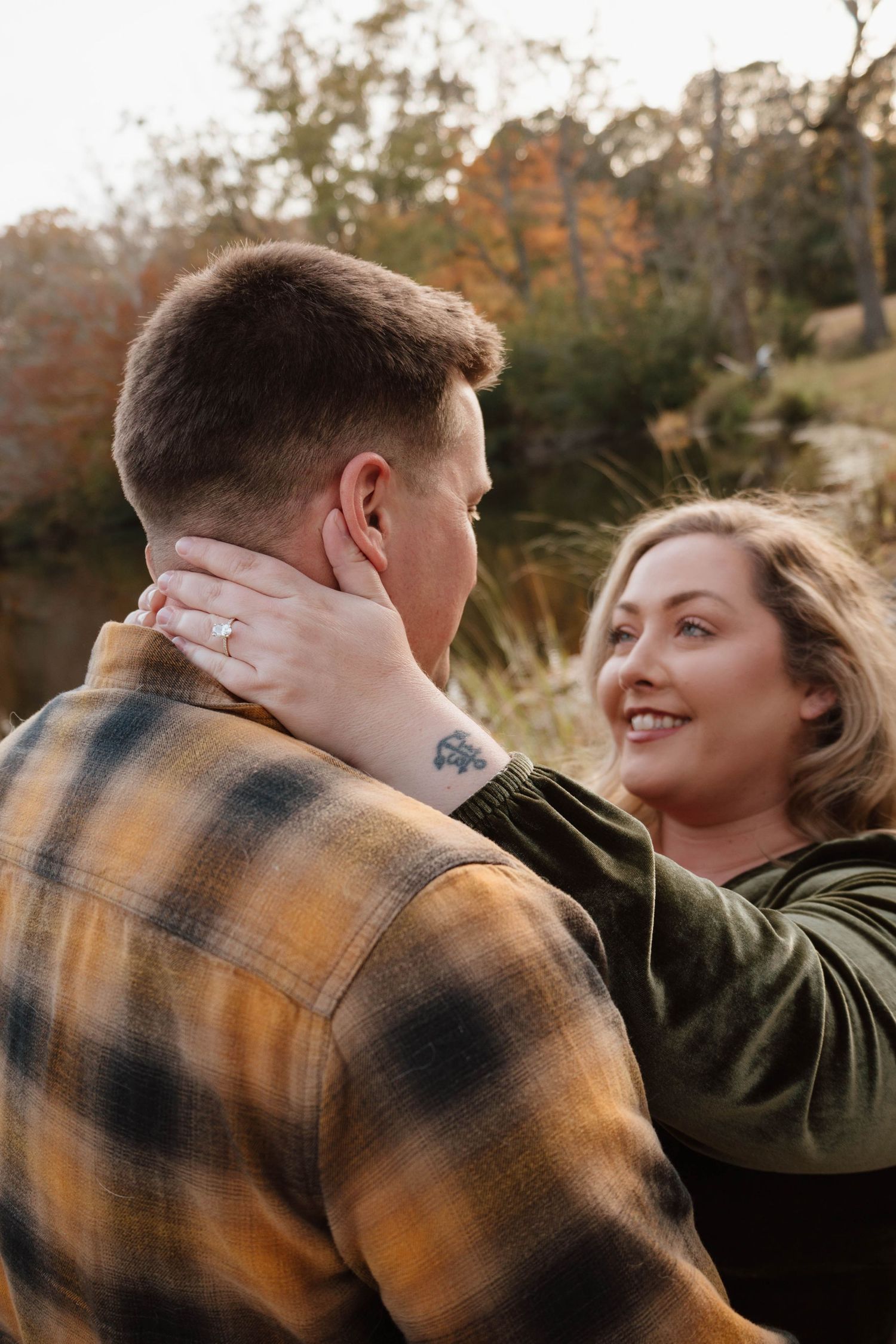 Romantic couple embracing outdoors wearing plaid and olive clothing.