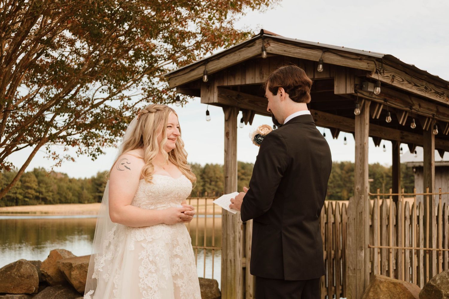 Couple shares a romantic moment under a rustic wooden pavilion during golden hour at their outdoor wedding.