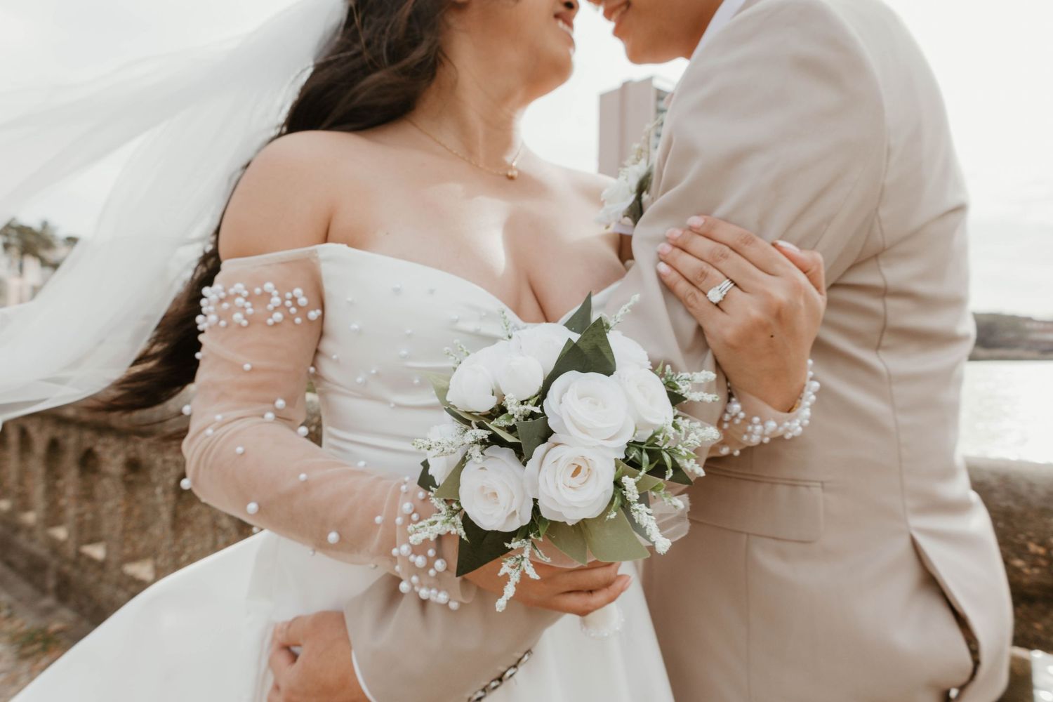 A bride and groom embrace tenderly, the bride holding a bouquet of white flowers.