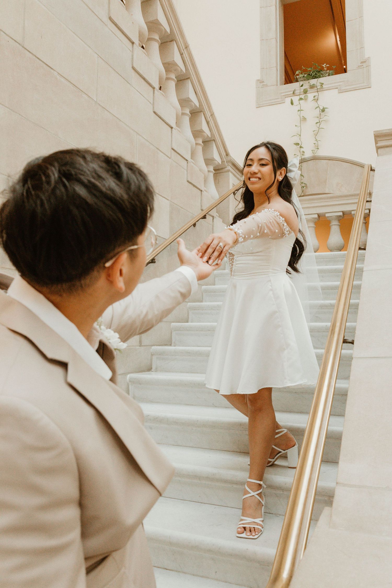 A woman in a white dress stands on a staircase, interacting with a man in a suit.