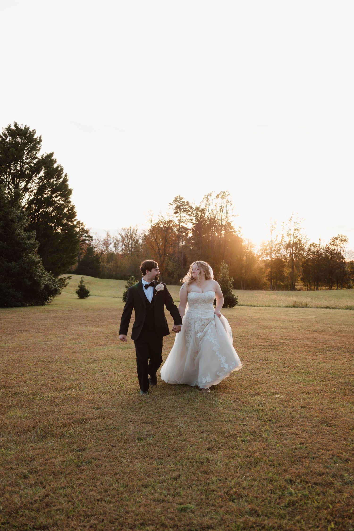 Newlyweds walking together in an open field during golden hour.