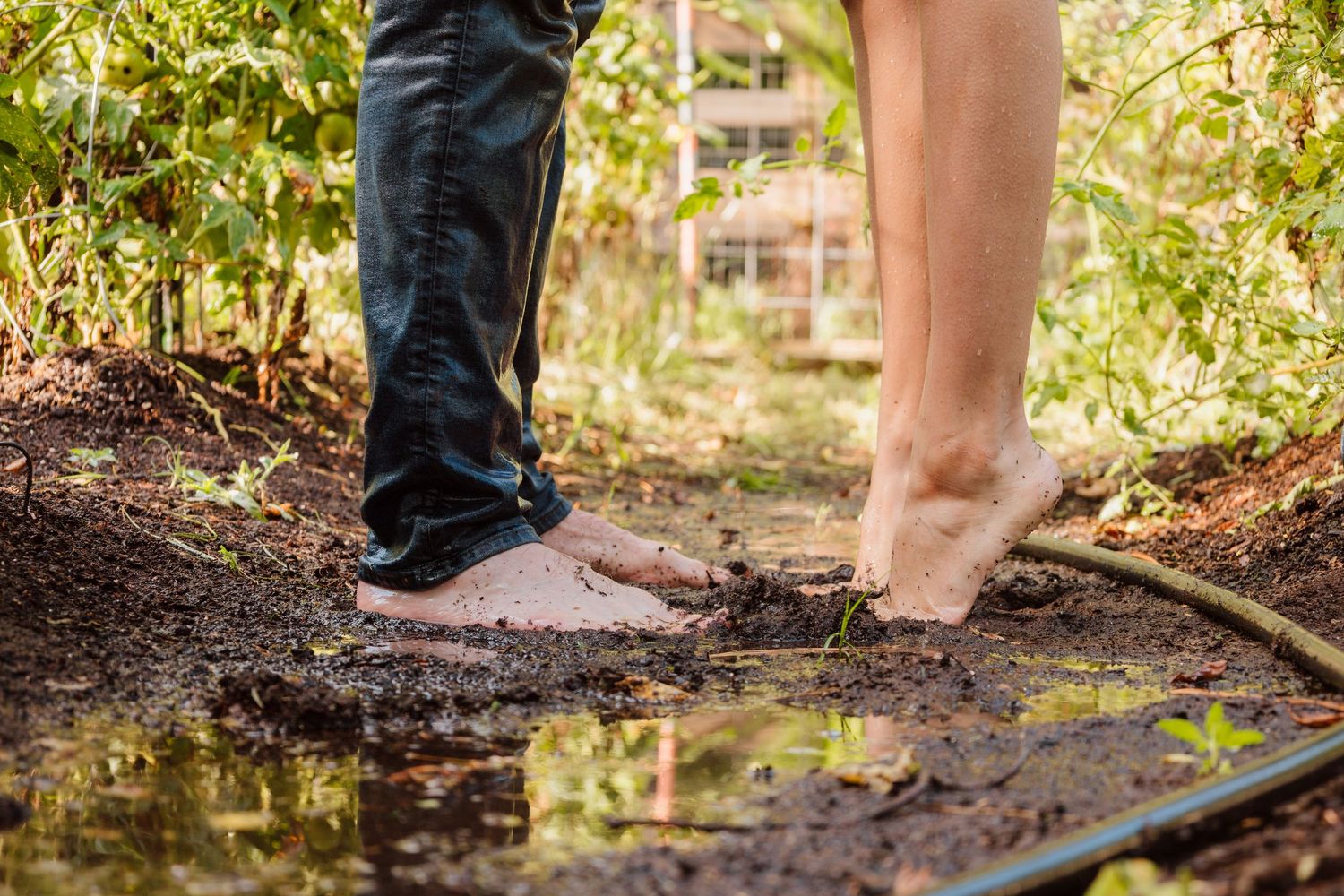 Close-up of two pairs of feet standing near a puddle in a garden path.