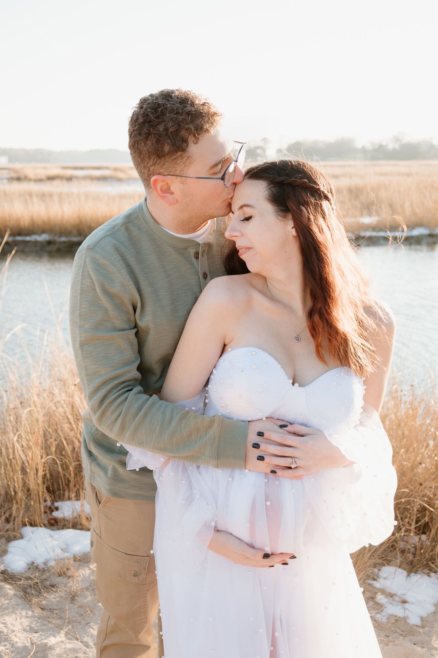 Romantic winter photo shoot in a field of tall grass with warm sunlight and snow patches.